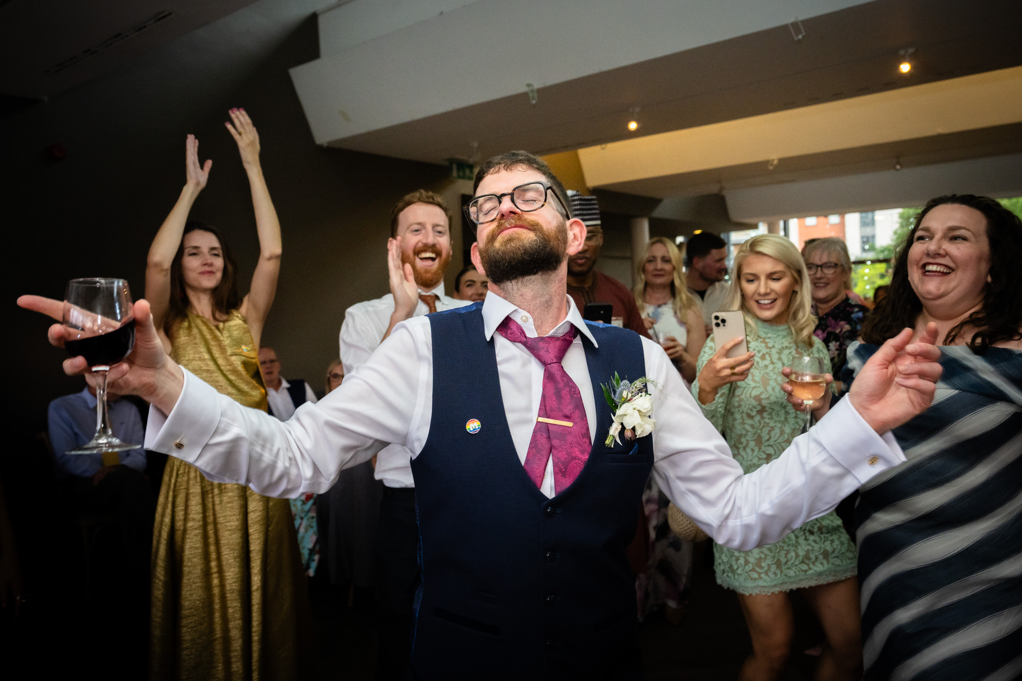 A guest in a grey suit crouches down on the dance floor with a big smile, fully enjoying the party atmosphere at Castlefield Rooms.