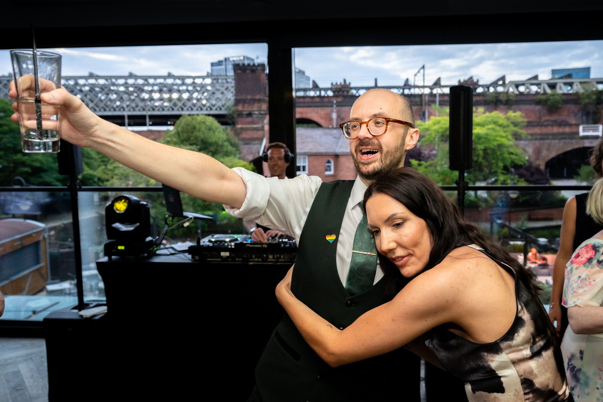 Wedding at Castlefield Rooms. Guests dance and celebrate in a line, with arms outstretched, his shirt covered in red wine stains during the evening party.
