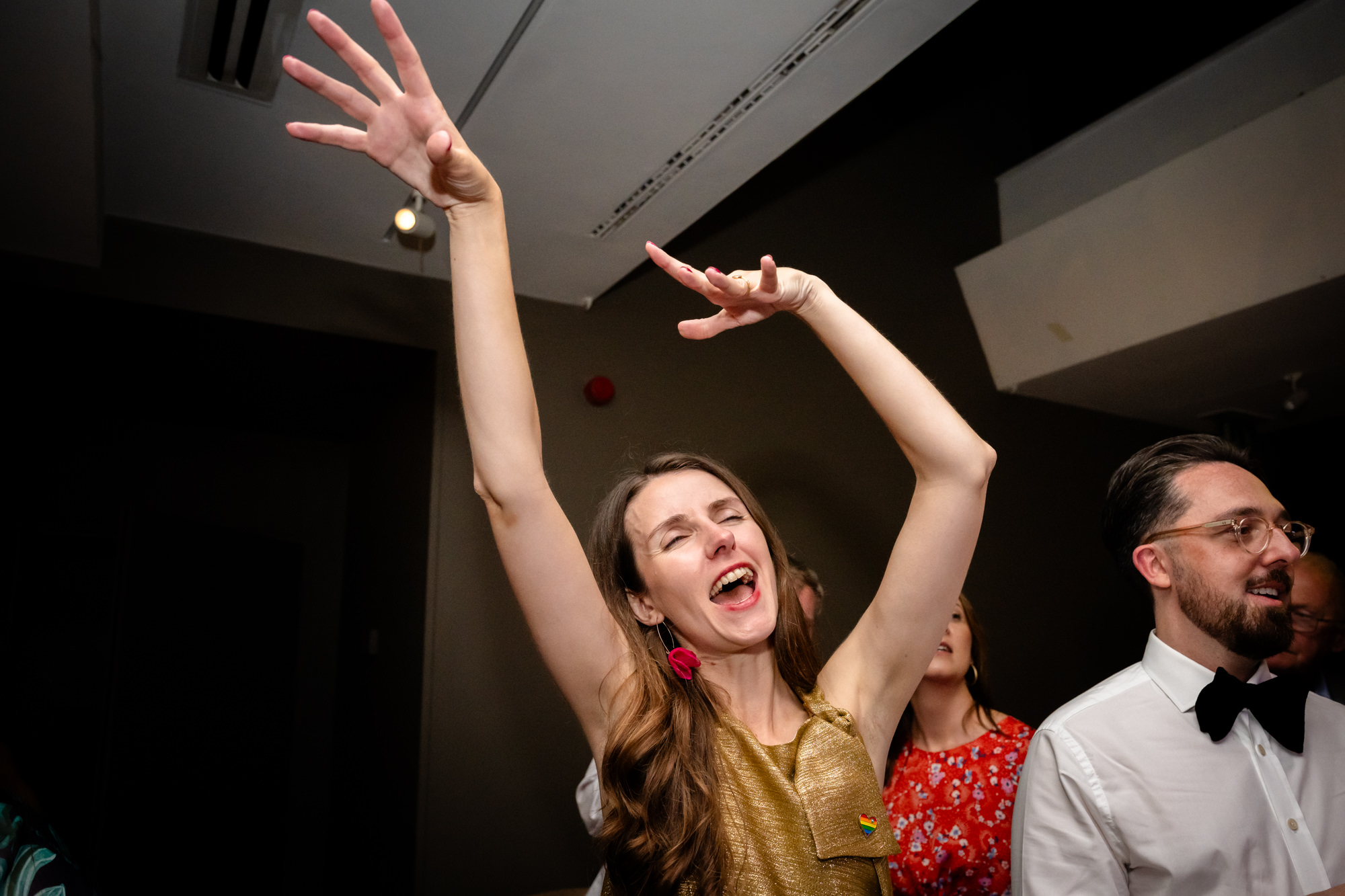 Wedding at Castlefield Rooms. A guest throws her arms up and cheers with a joyful expression while dancing at the evening party.