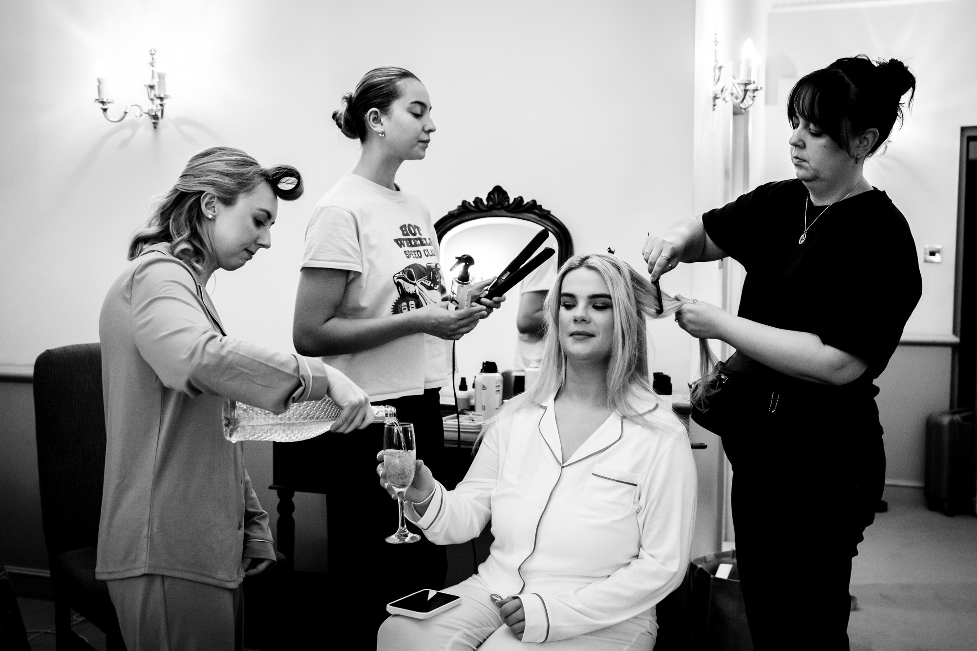 Black and white photo of a stylist applying hairspray to the bride while bridesmaids assist during bridal wedding prep at Nunsmere Hall.