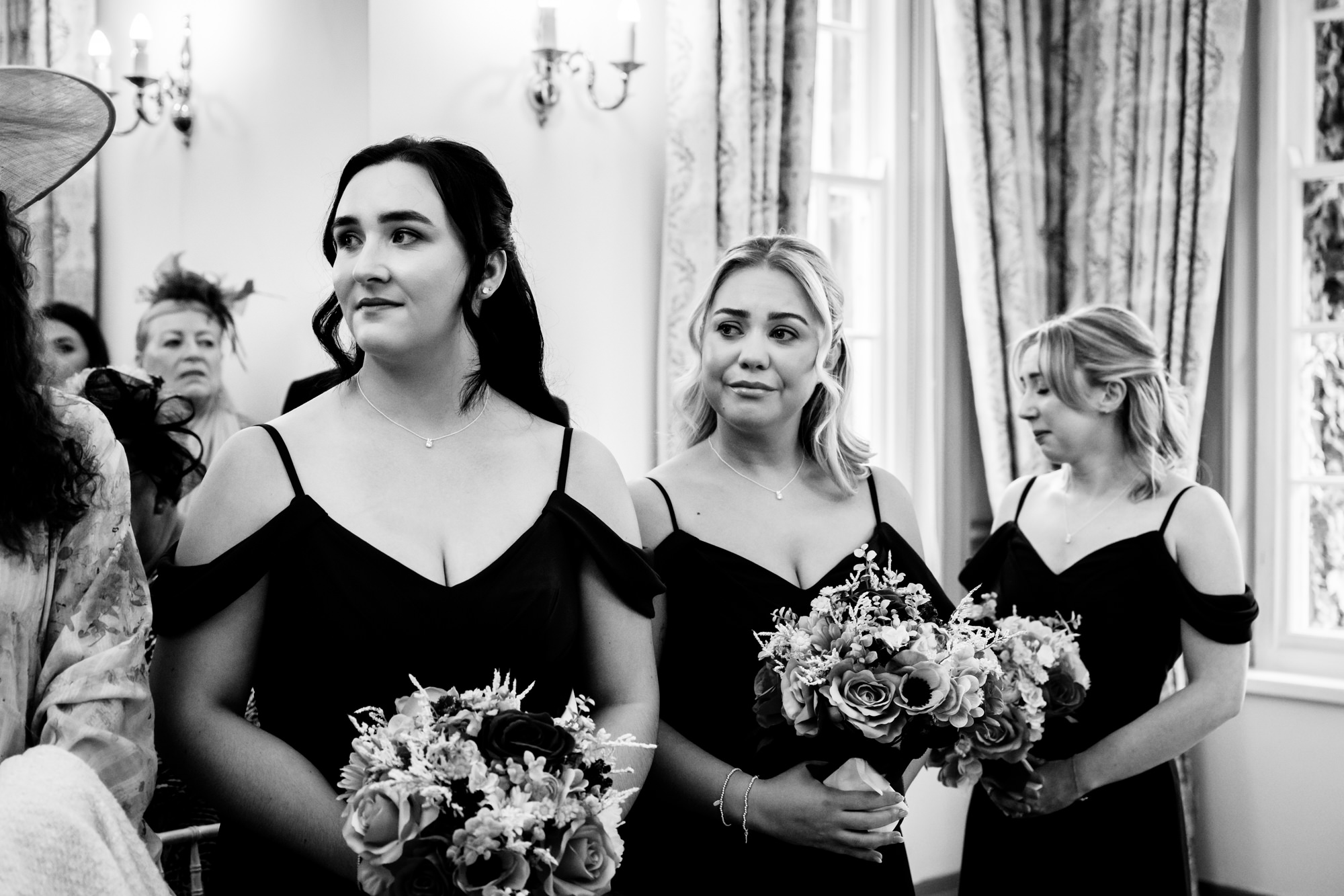 Three bridesmaids in black off the shoulder dresses standing at the front of the ceremony room at Nunsmere Hall.