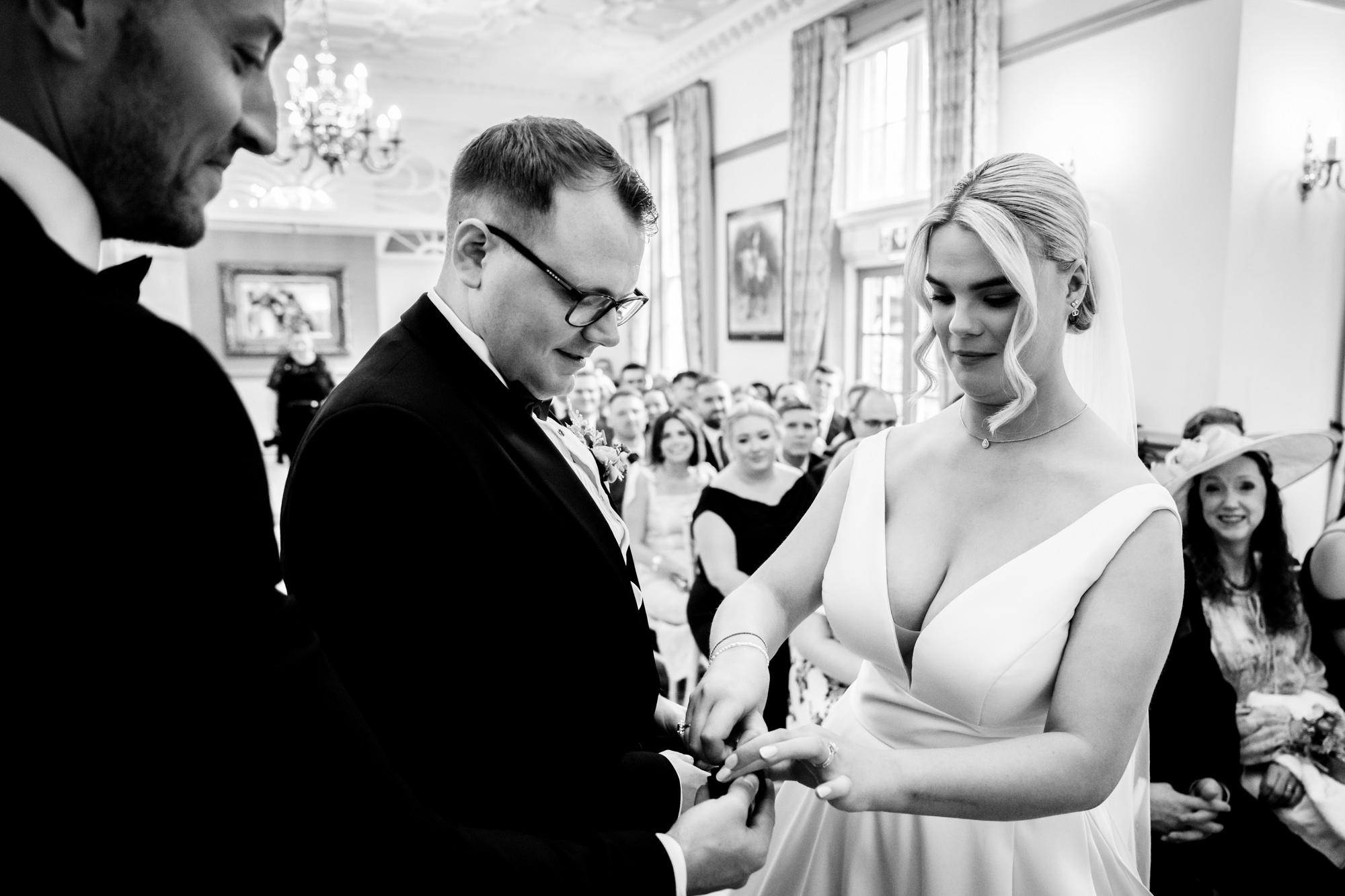 The bride placing the wedding ring on the groom finger during the exchange of rings at Nunsmere Hall.