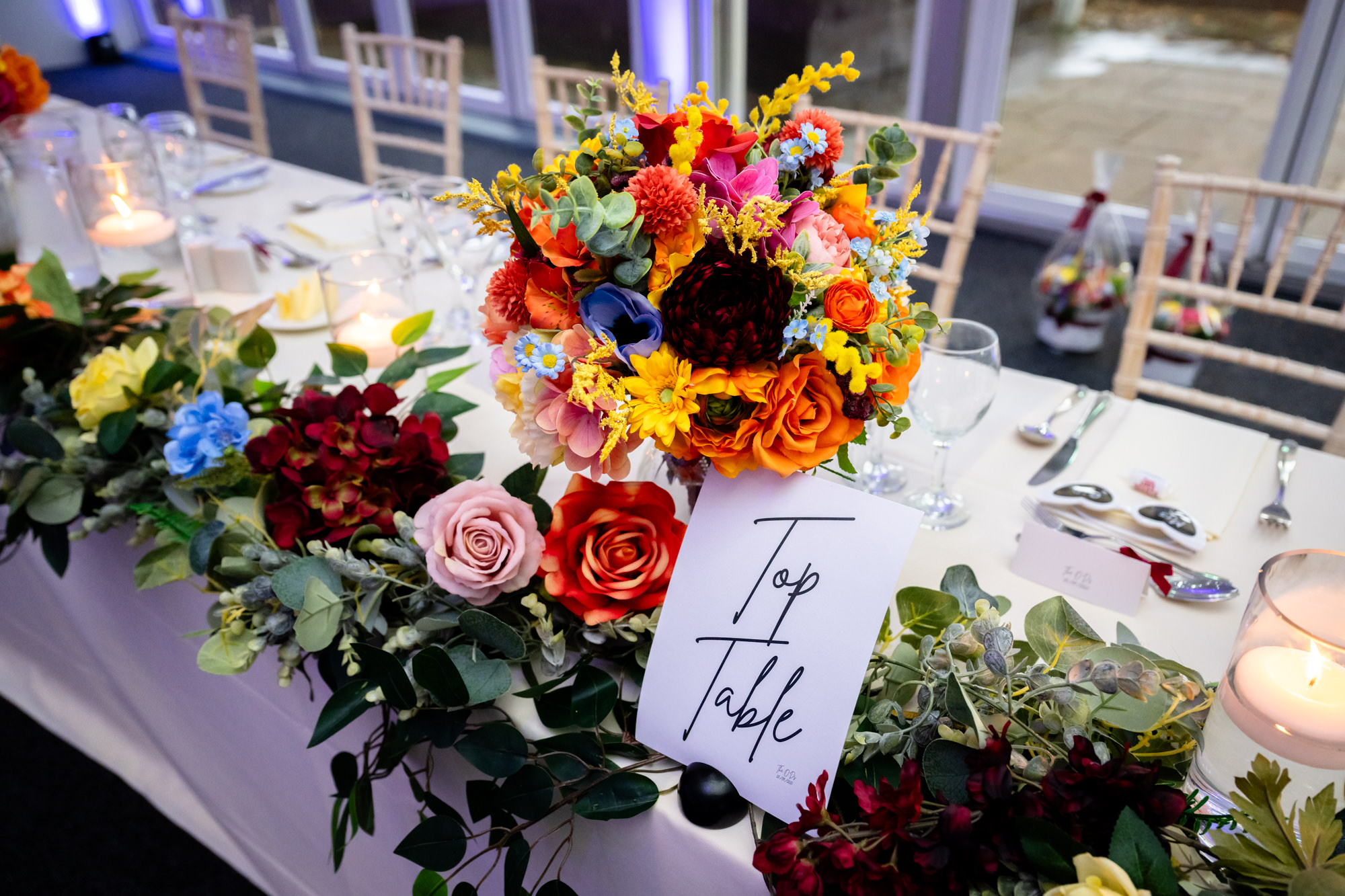 Detail shot of the top table at Nunsmere Hall decorated with colourful roses and a sign reading Top Table.