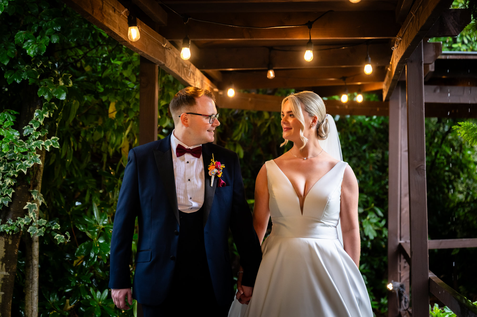 A night portrait of the couple smiling at each other under outdoor string lights at Nunsmere Hall.