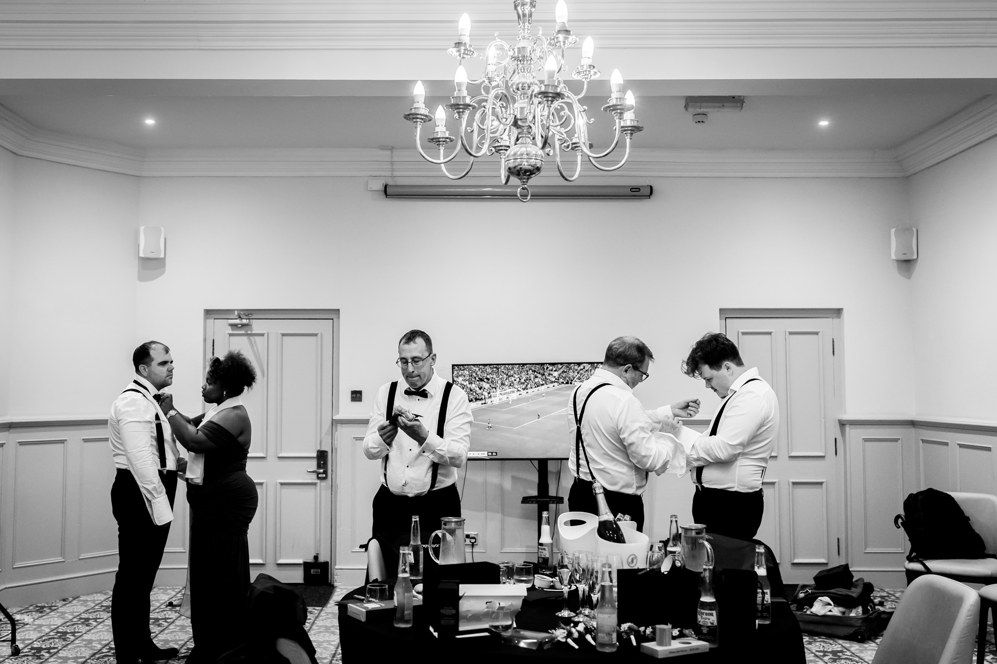 Groomsmen standing in a group adjusting their bow ties and suspenders at Nunsmere Hall.