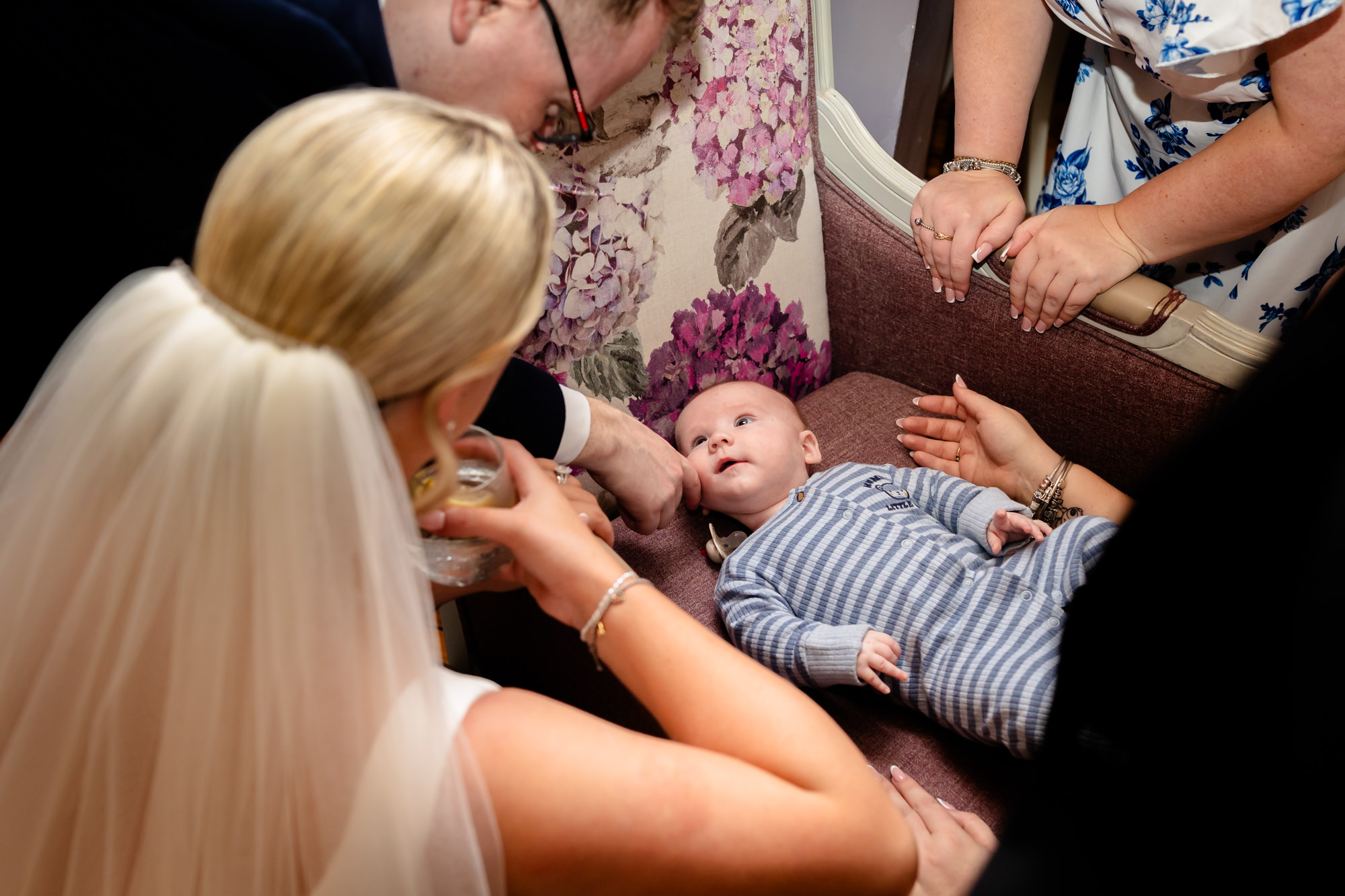 The bride smiling down at a baby lying on a chair at Nunsmere Hall.