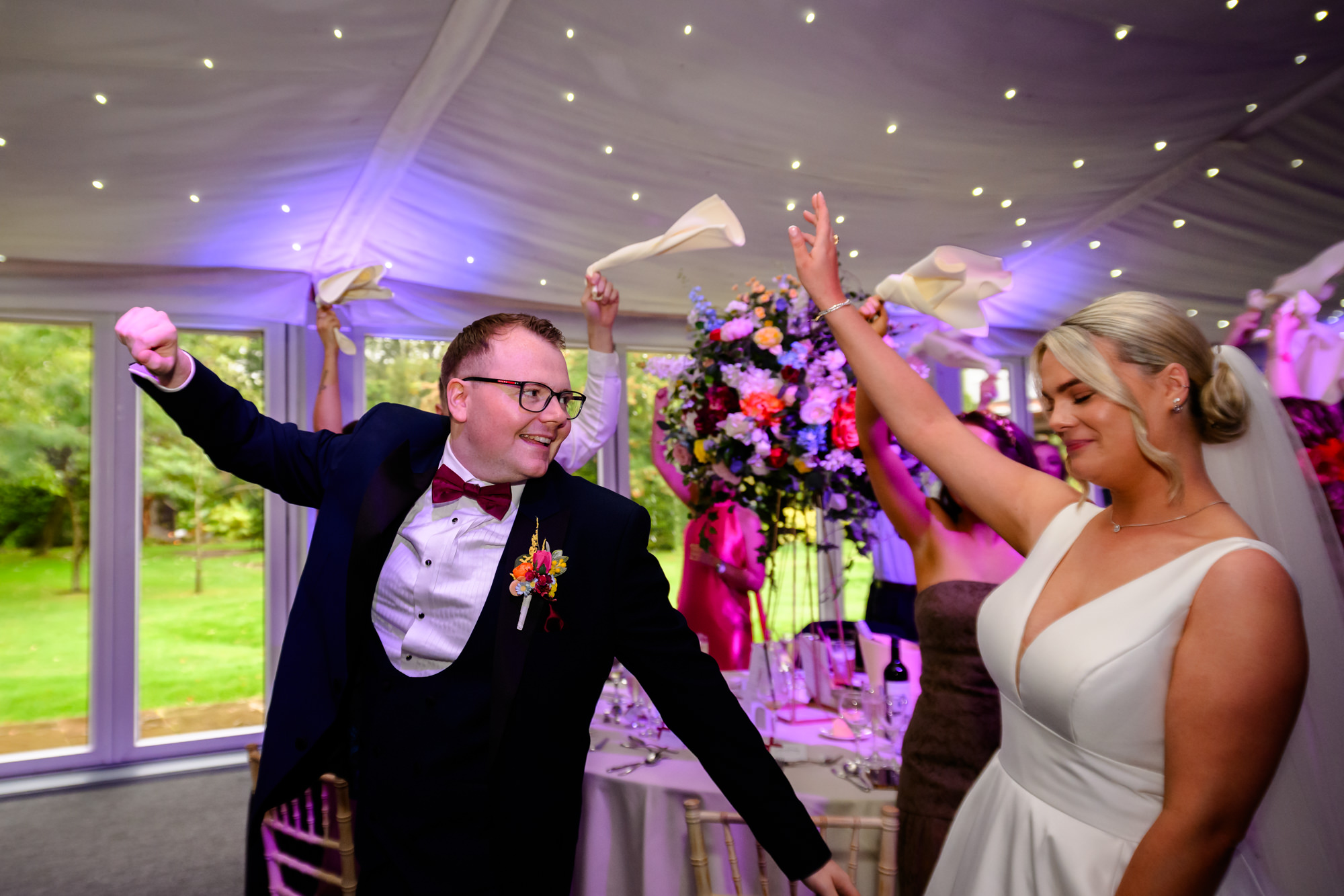 The groom cheering with his arms raised as the couple enters the wedding breakfast at Nunsmere Hall.