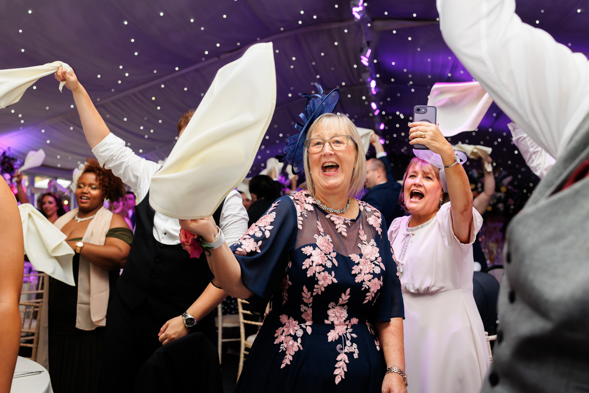 Older guests laughing and waving napkins in celebration at Nunsmere Hall.