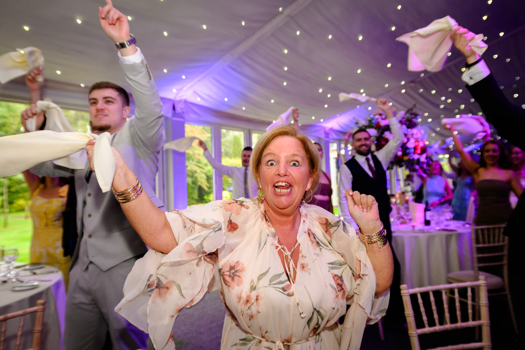 Wedding guests standing and cheering with napkins in the air during the reception entrance at Nunsmere Hall.