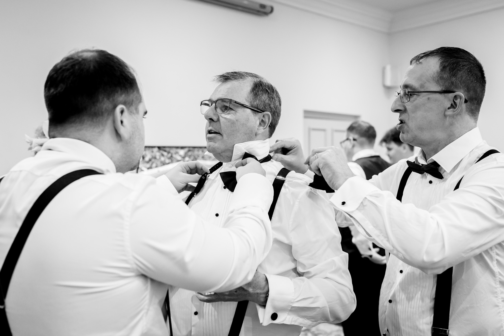 A close up black and white shot of groomsmen helping each other with their bow ties at Nunsmere Hall.