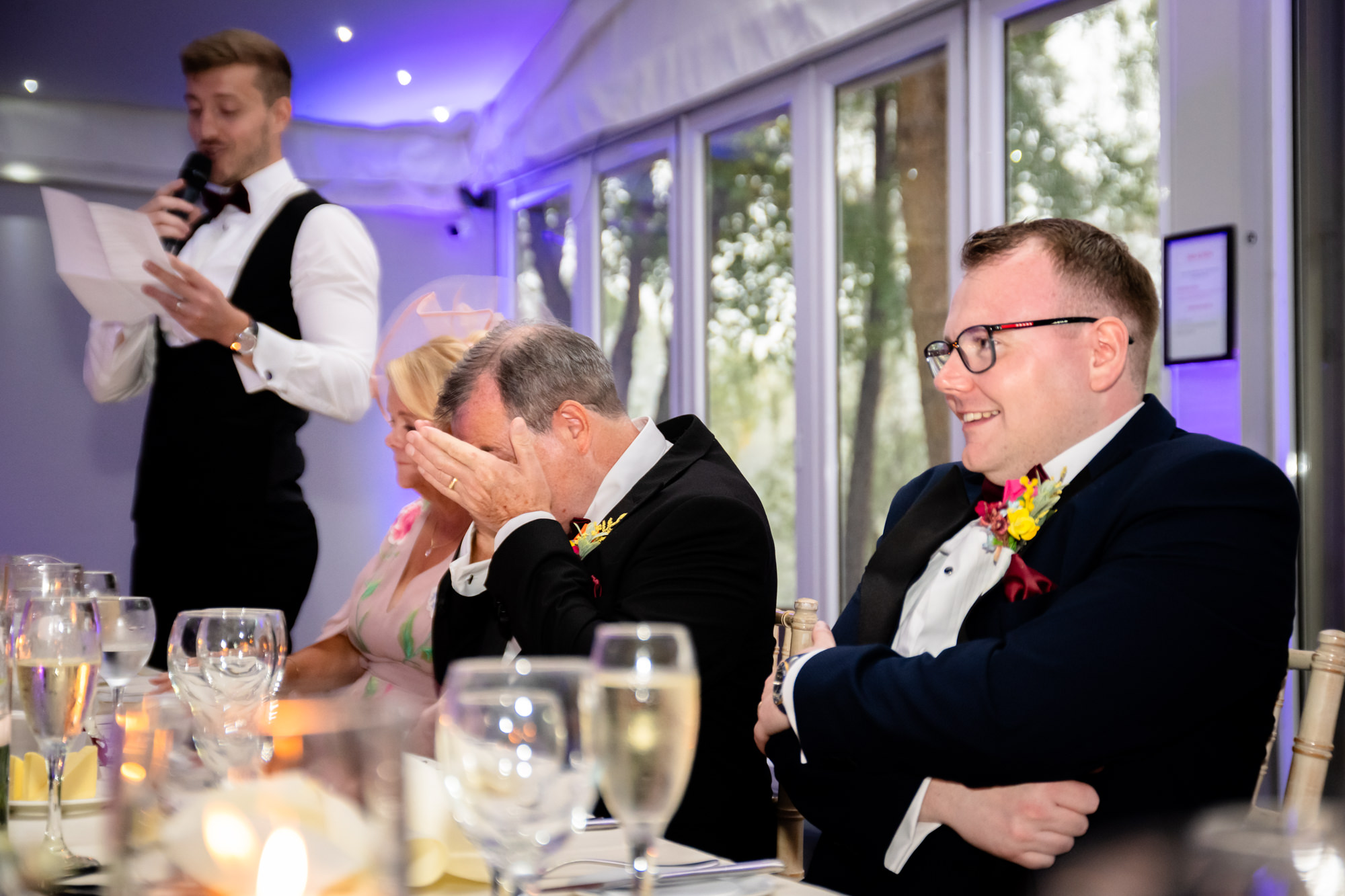 The father of the groom is laughing with his head in his hands during the best man speech at Nunsmere Hall.