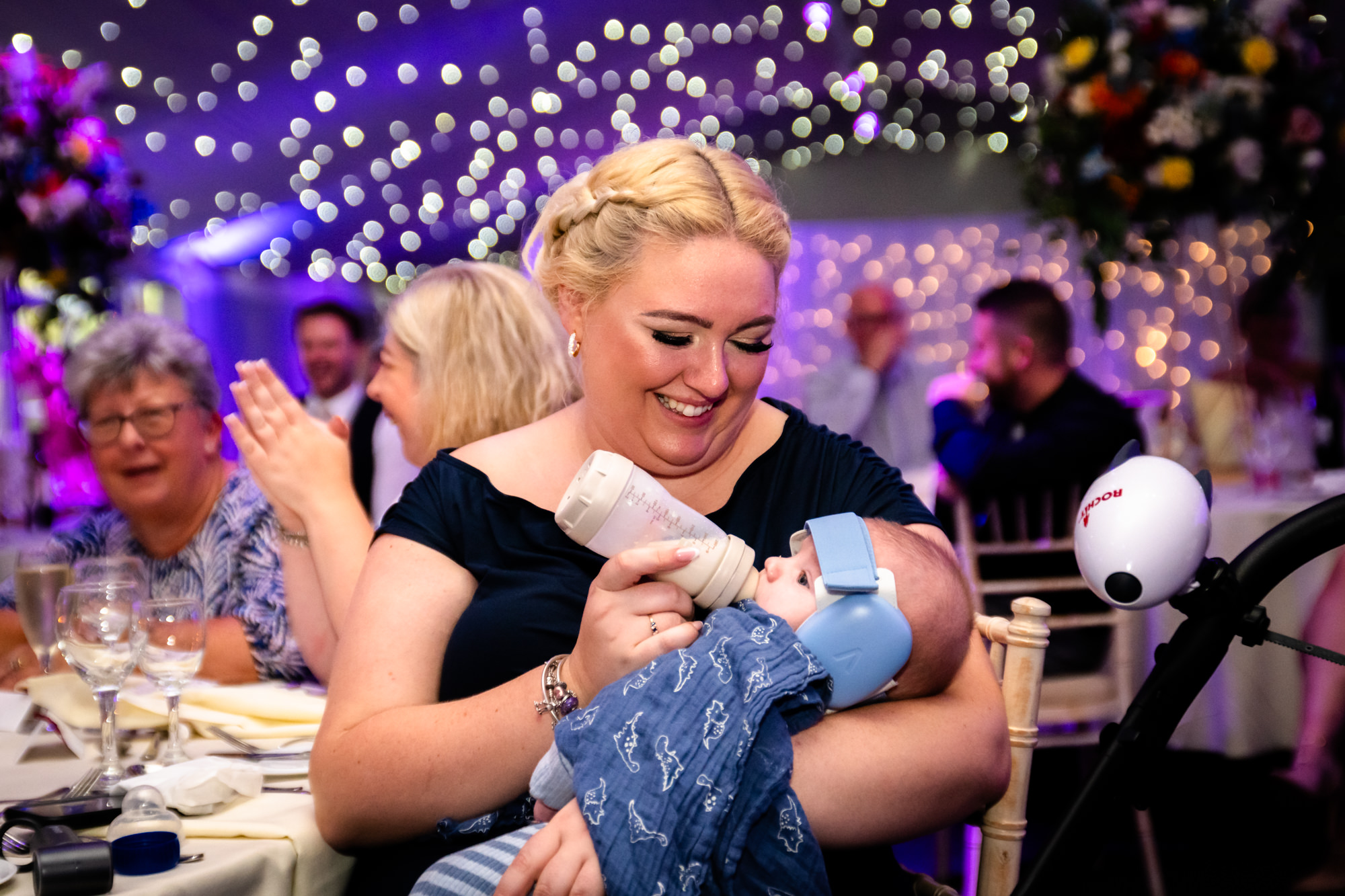 A guest feeding a baby a bottle of milk at the dinner table at Nunsmere Hall.