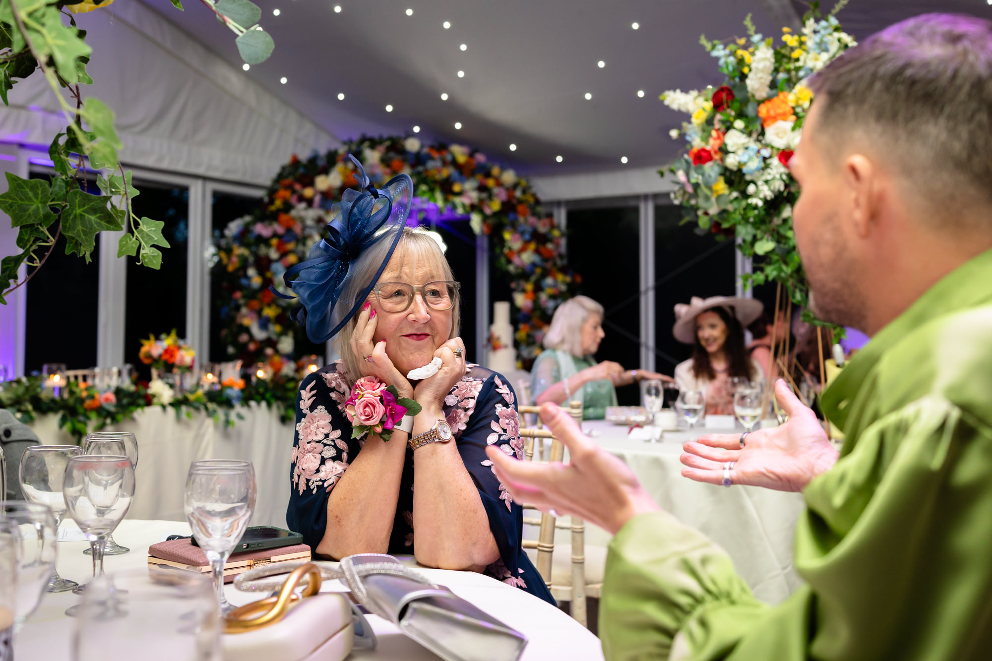 An older guest resting her chin on her hands while listening to the speeches at Nunsmere Hall.