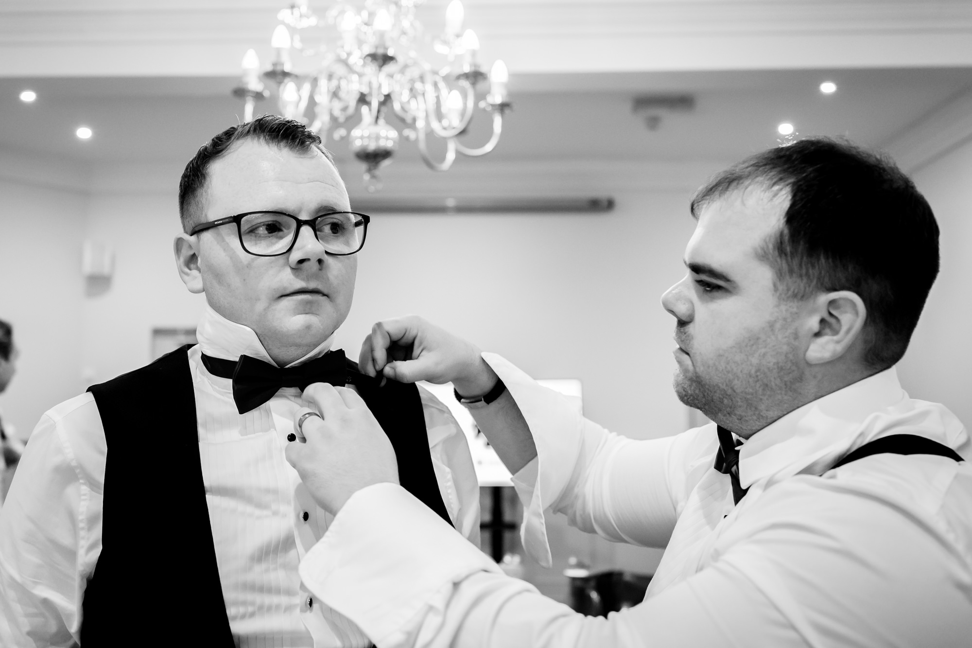 The groom having his black bow tie adjusted by his groomsman while preparing for the wedding at Nunsmere Hall.