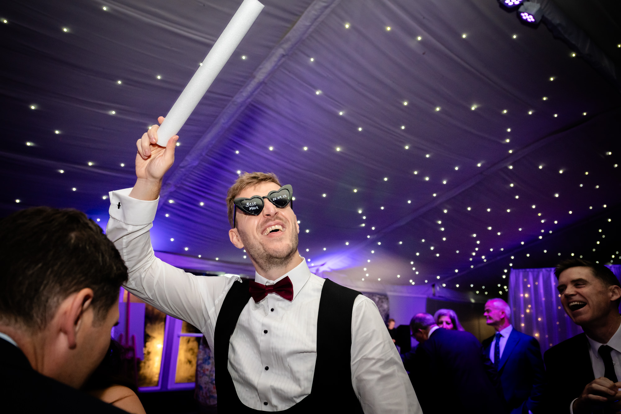 A guest wearing sunglasses waving a foam glow stick on the dance floor at Nunsmere Hall.