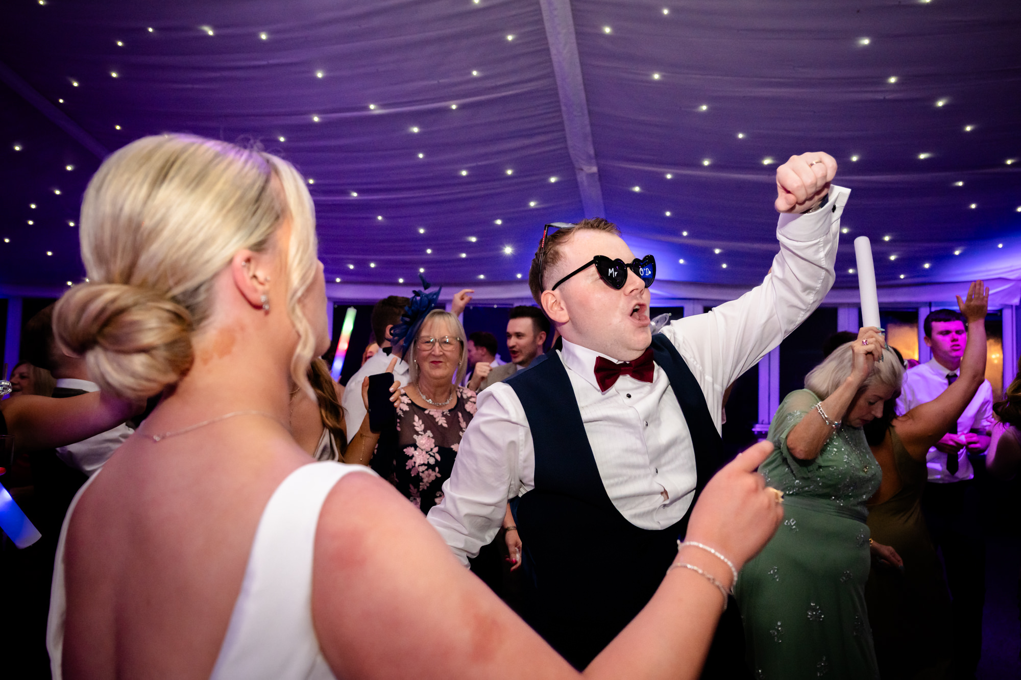 The groom wearing sunglasses and dancing with glow sticks at a wedding at Nunsmere Hall.