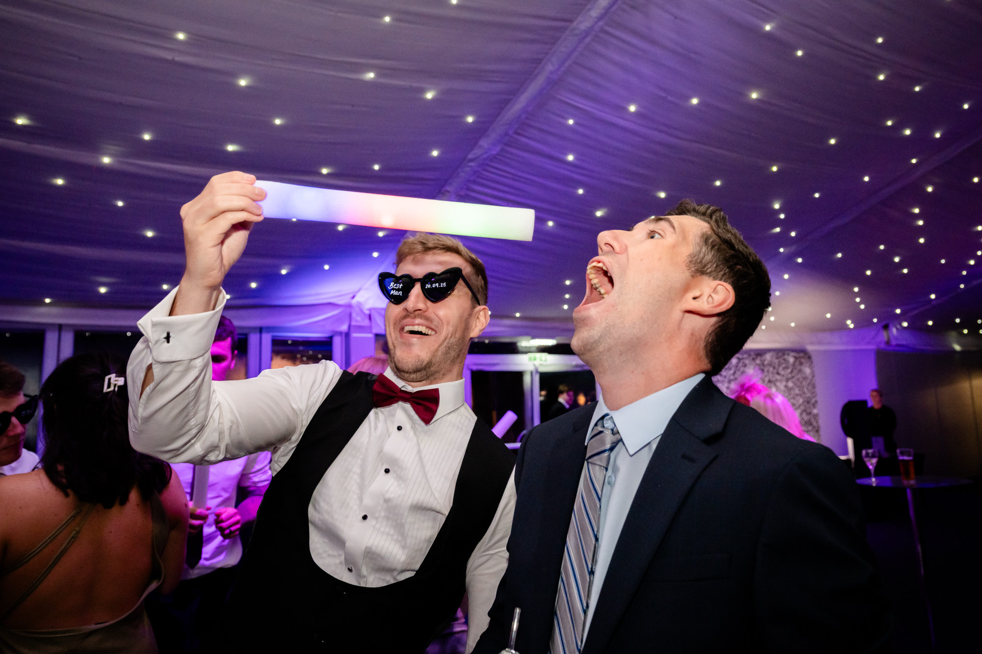 The groom and a guest dancing under the purple party lights at Nunsmere Hall.