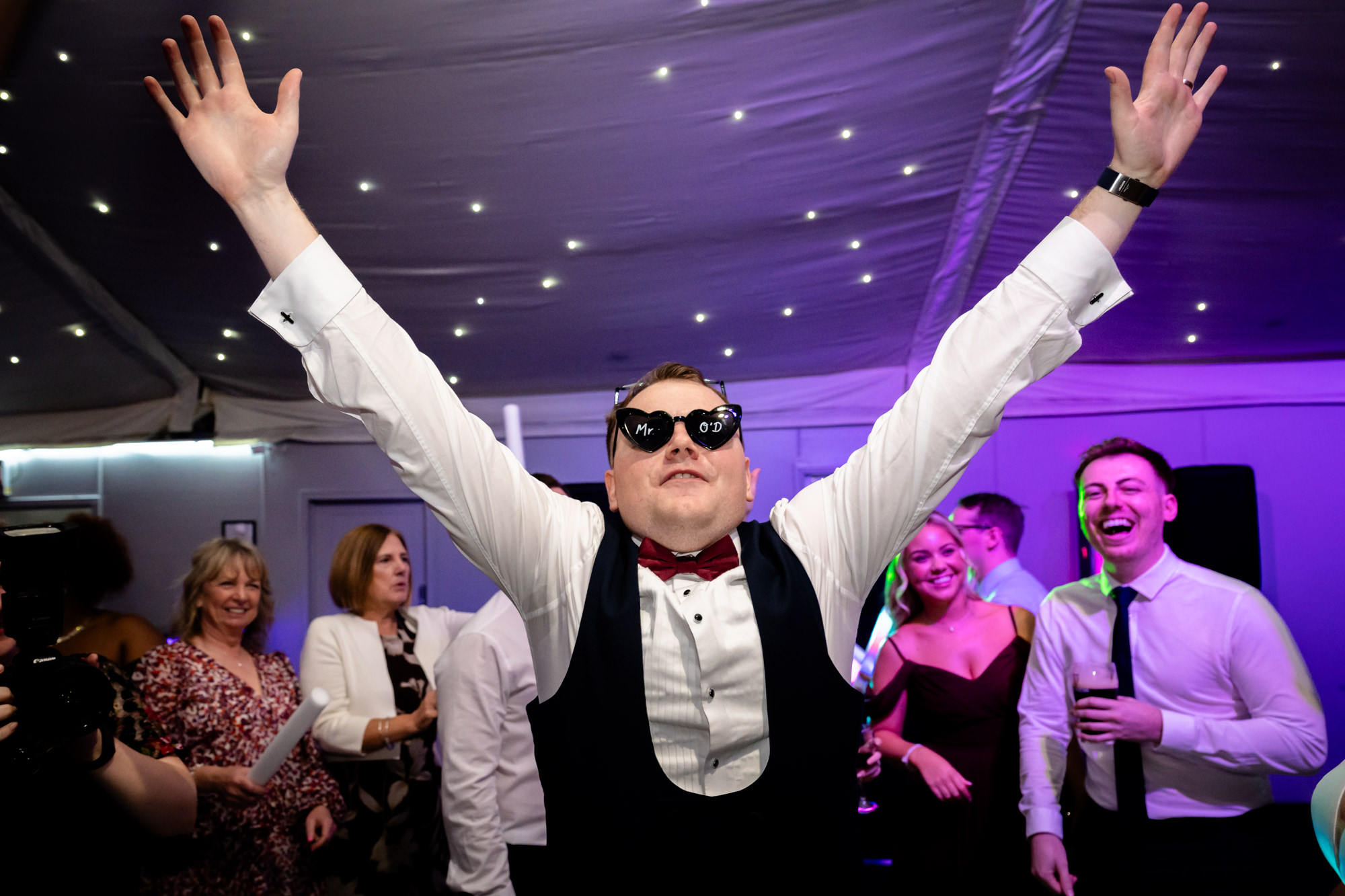The groom holding his arms open wide while dancing with guests at Nunsmere Hall.