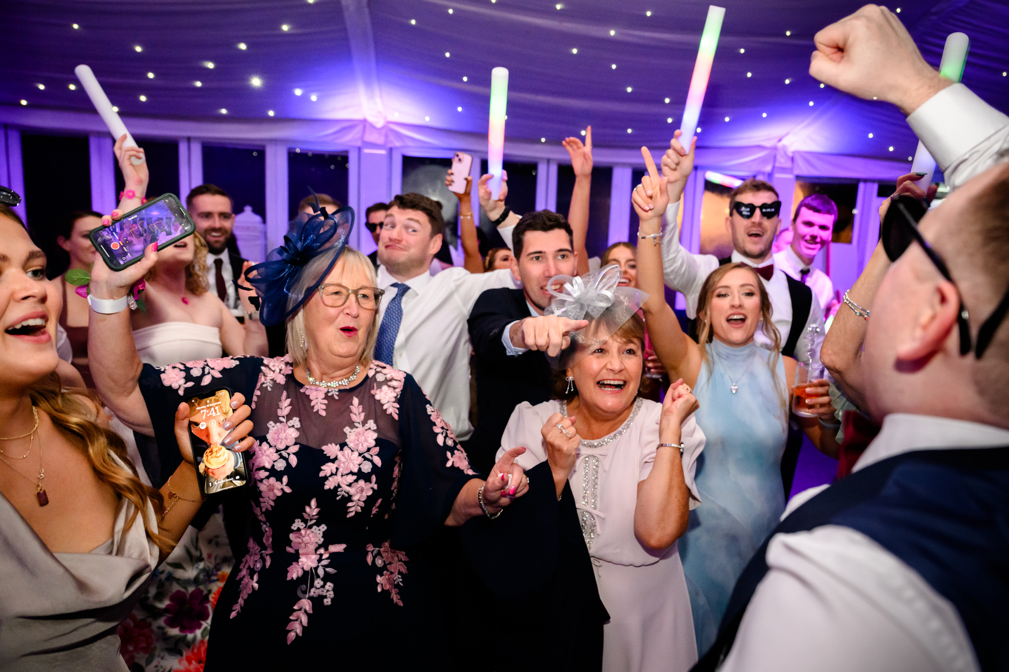 A crowded dance floor with guests waving glow sticks at a wedding at Nunsmere Hall.
