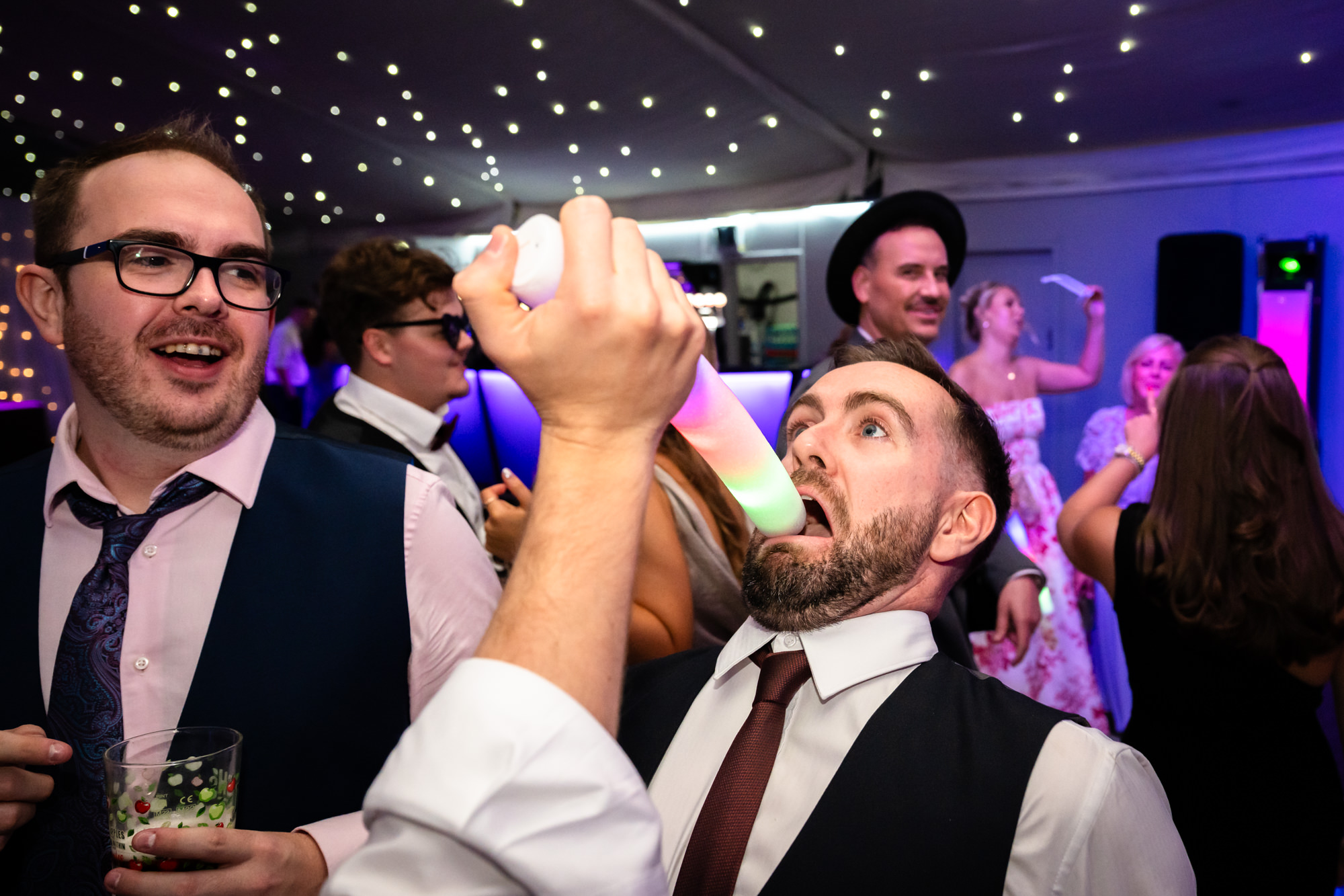 Guests shoving a glow stick in someone's mouth on the dance floor at Nunsmere Hall.
