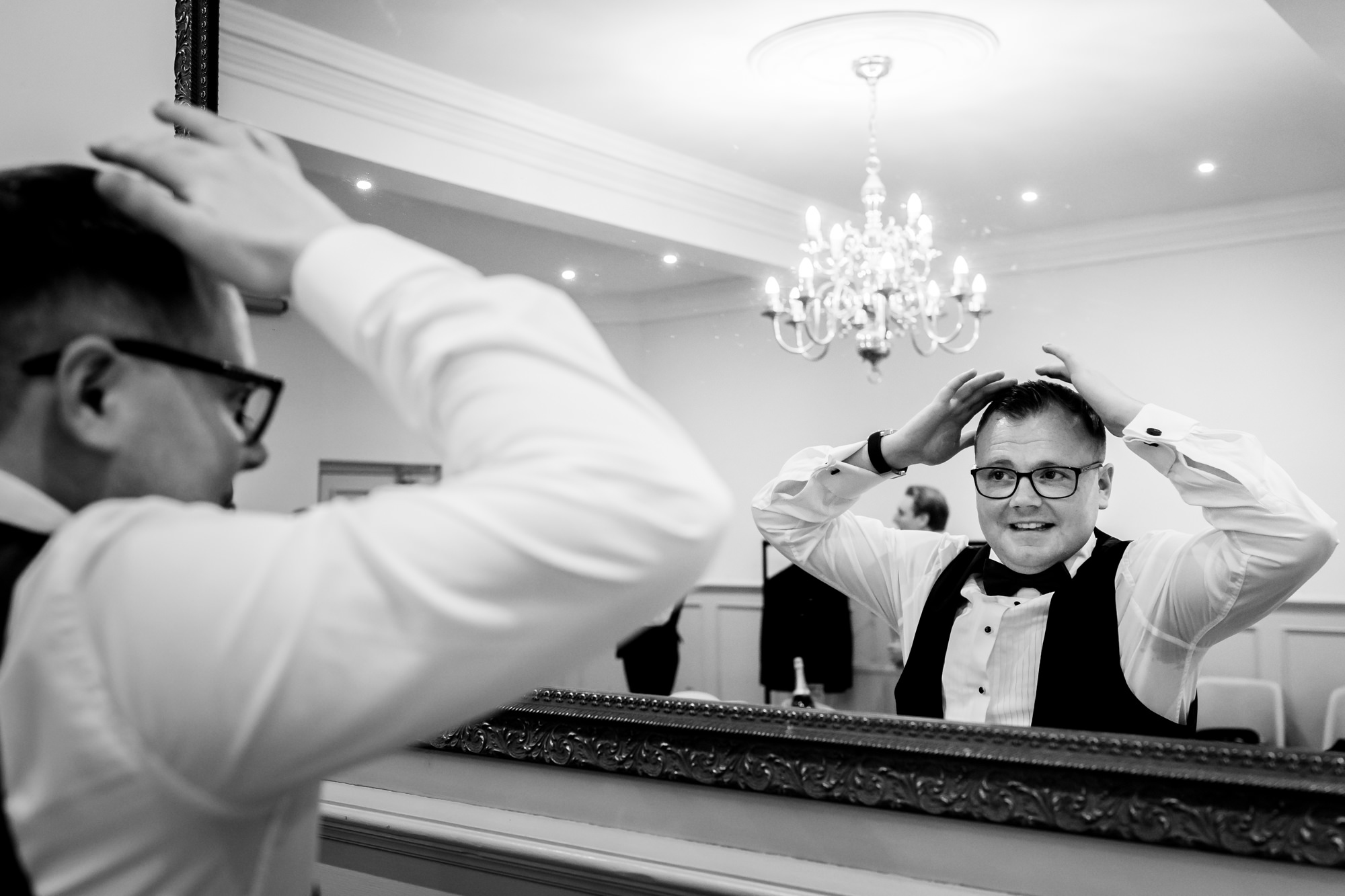 The groom checking his hair and glasses in a large mirror during a wedding at Nunsmere Hall.
