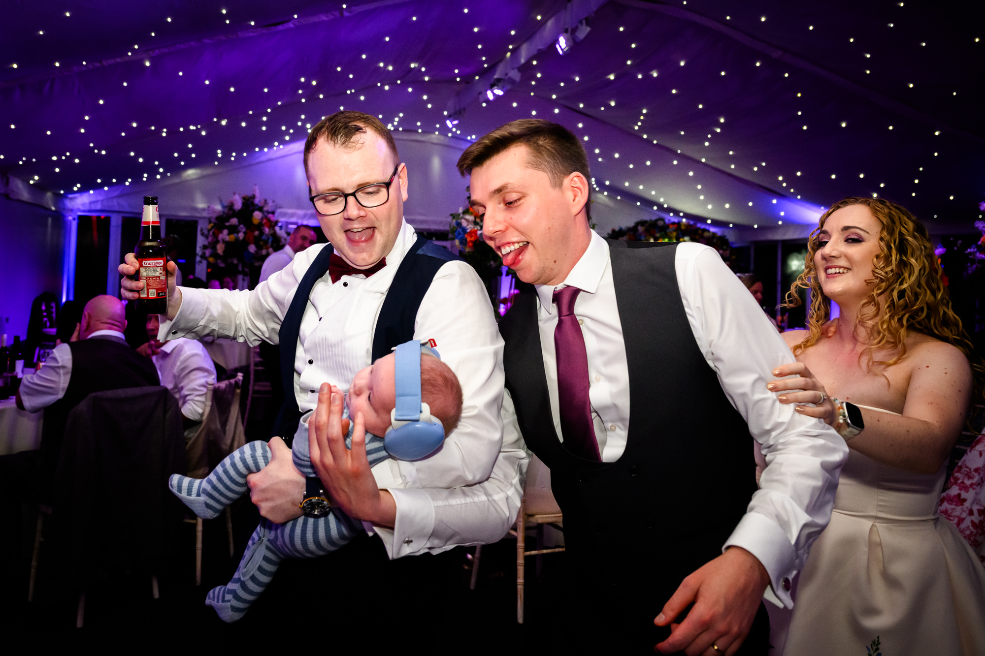 The groom holding his baby with one hand, in a conga line at Nunsmere Hall.