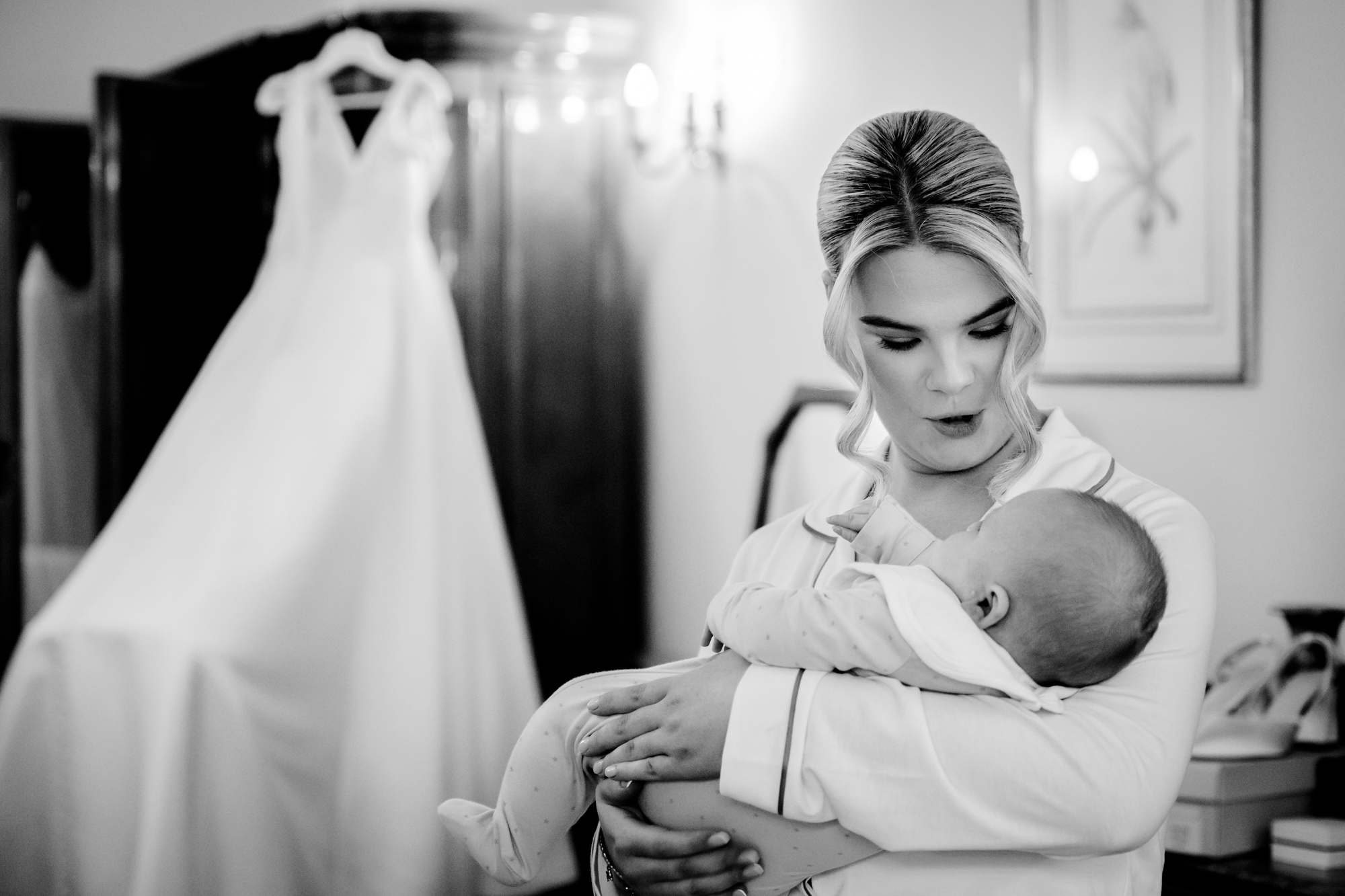 Black and white shot of the bride in her pyjamas gently holding a baby at Nunsmere Hall.