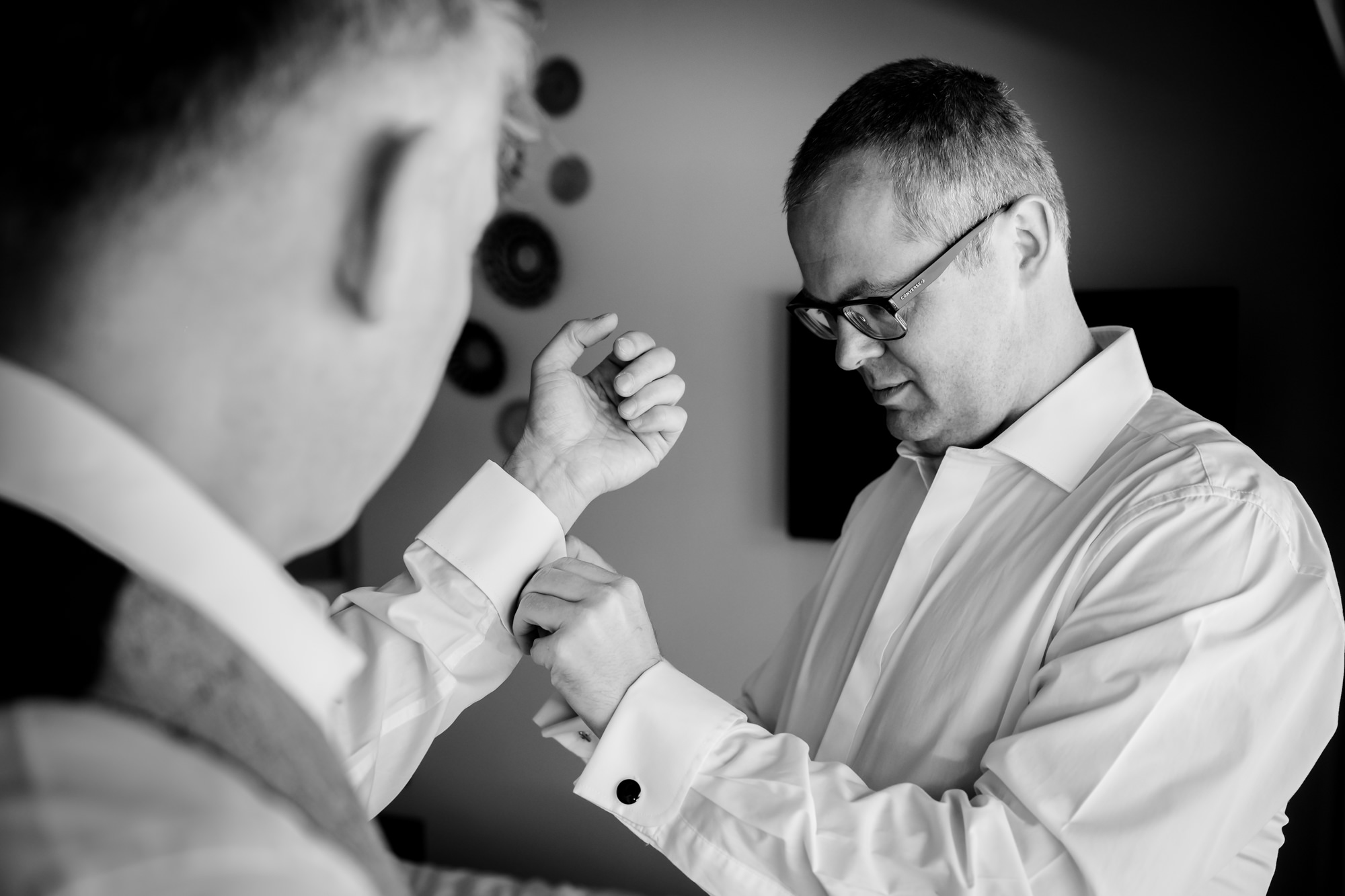 Dom fastens his cufflinks with a hand from a friend while getting ready.