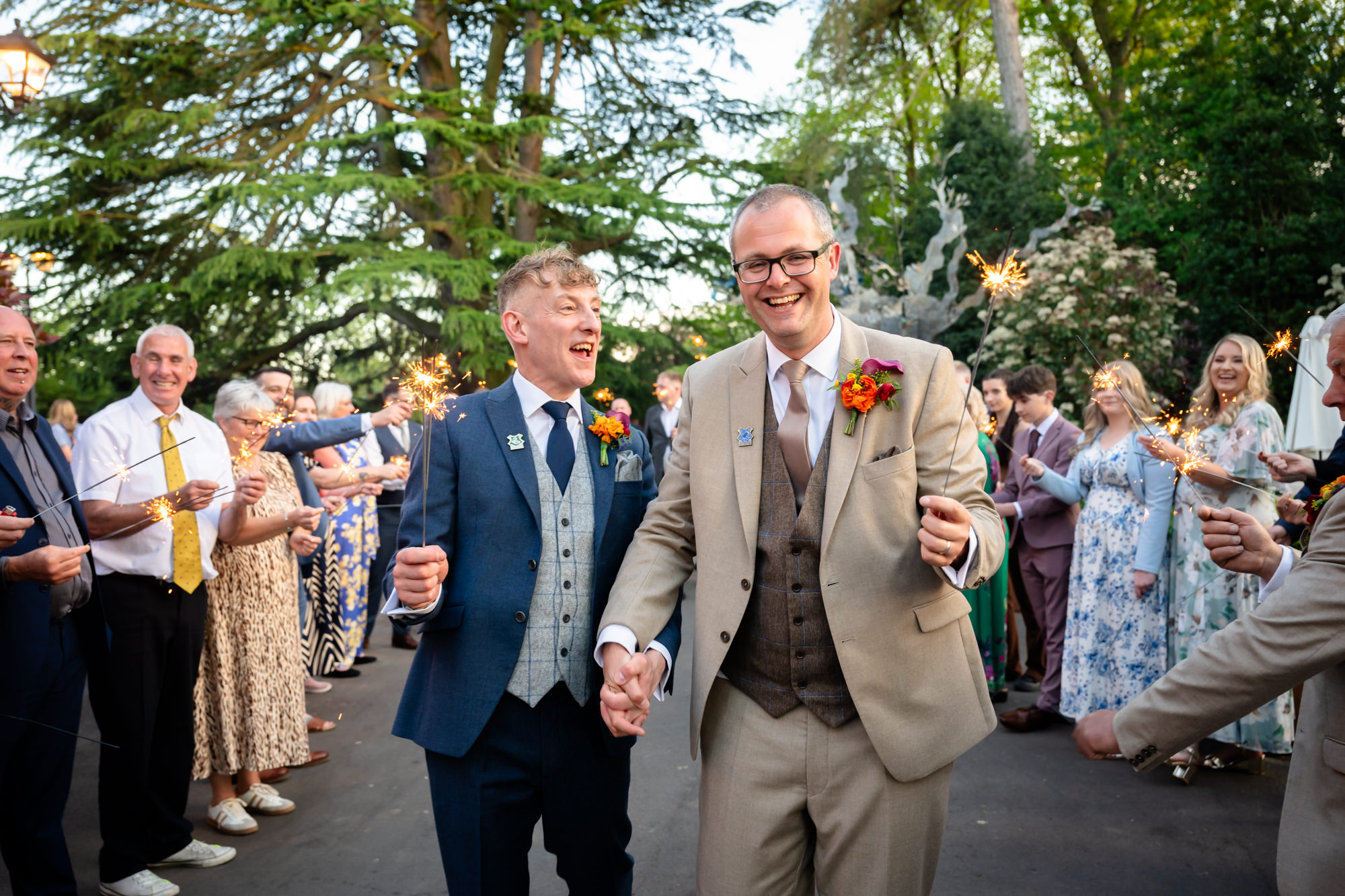 Marc and Dom walk hand in hand through a sparkler send-off in the evening light at The Oakfield.