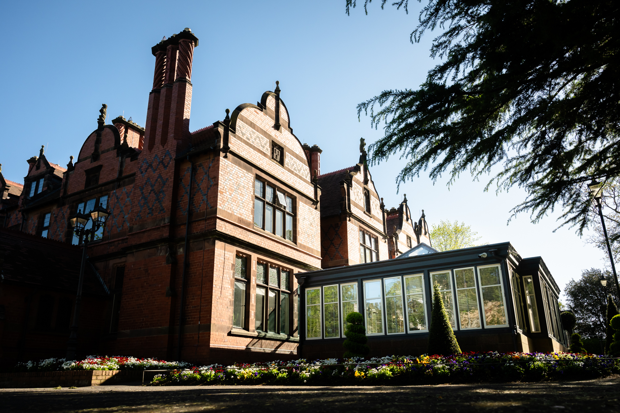 The Oakfield at Chester Zoo with the Orangery extension visible on the right, set against a clear blue sky and colourful flower beds