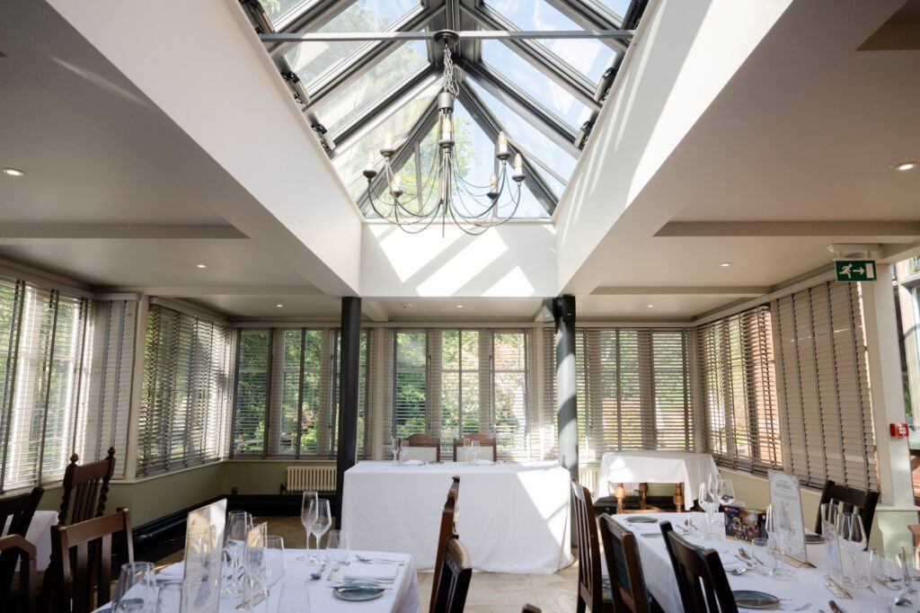 Interior of the Orangery at Chester Zoo looking up toward the glass skylight lantern roof and chandelier, with wedding breakfast tables set below