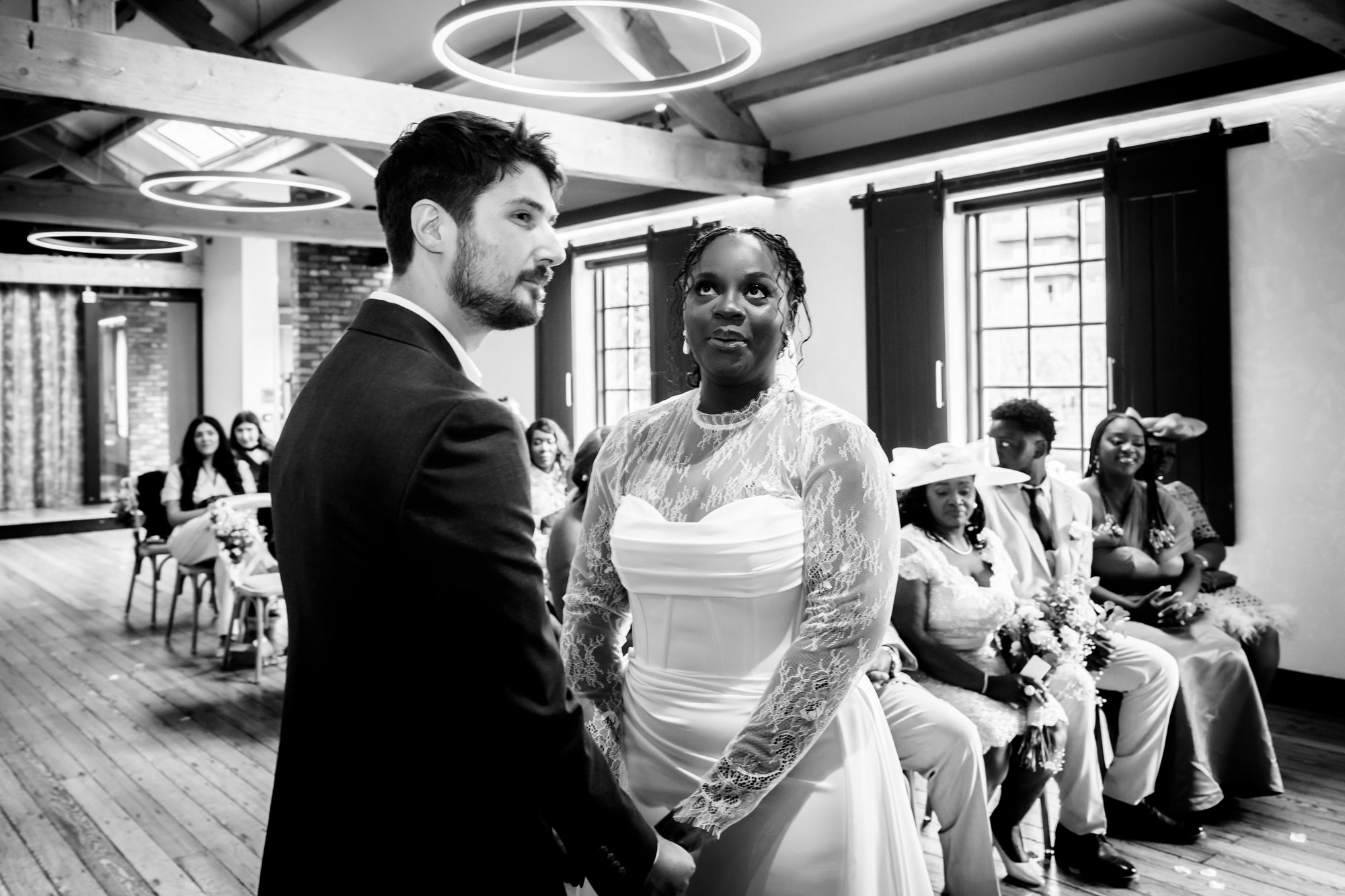 Black and white candid of the bride and groom holding hands at the altar during their wedding ceremony in the Brindley Room at The Castlefield Rooms.