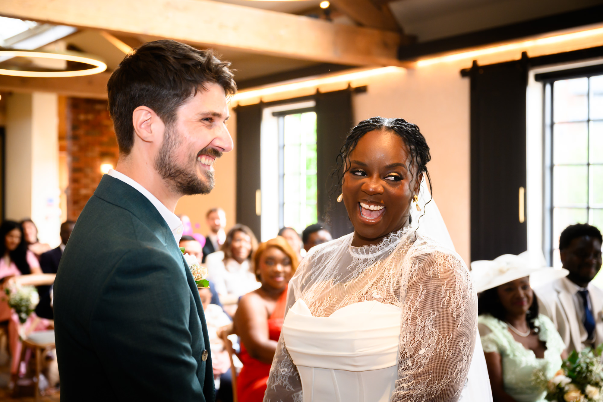 The bride laughing with the groom at the altar during their wedding ceremony in the Brindley Room at The Castlefield Rooms, with guests smiling in the background.