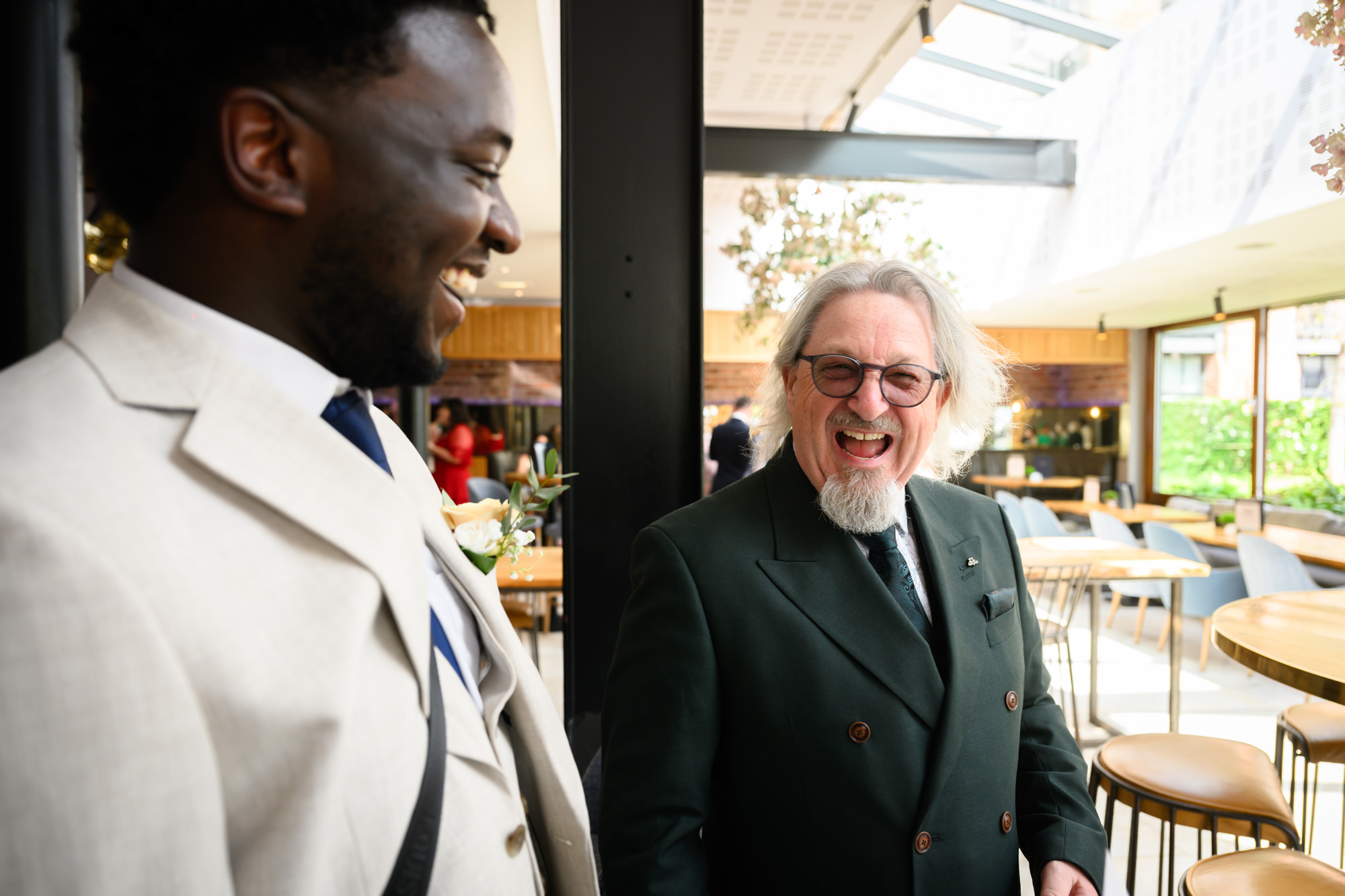 A guest in a cream suit laughing with an older male guest at The Castlefield Rooms ahead of the wedding ceremony.