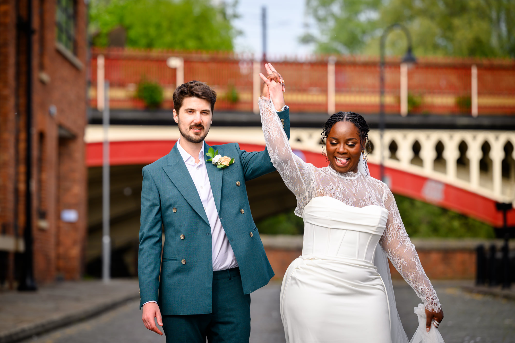 The bride spinning as the groom raises her hand on the cobbled streets of Castlefield during their wedding portrait session, with the red railway viaduct in the background.