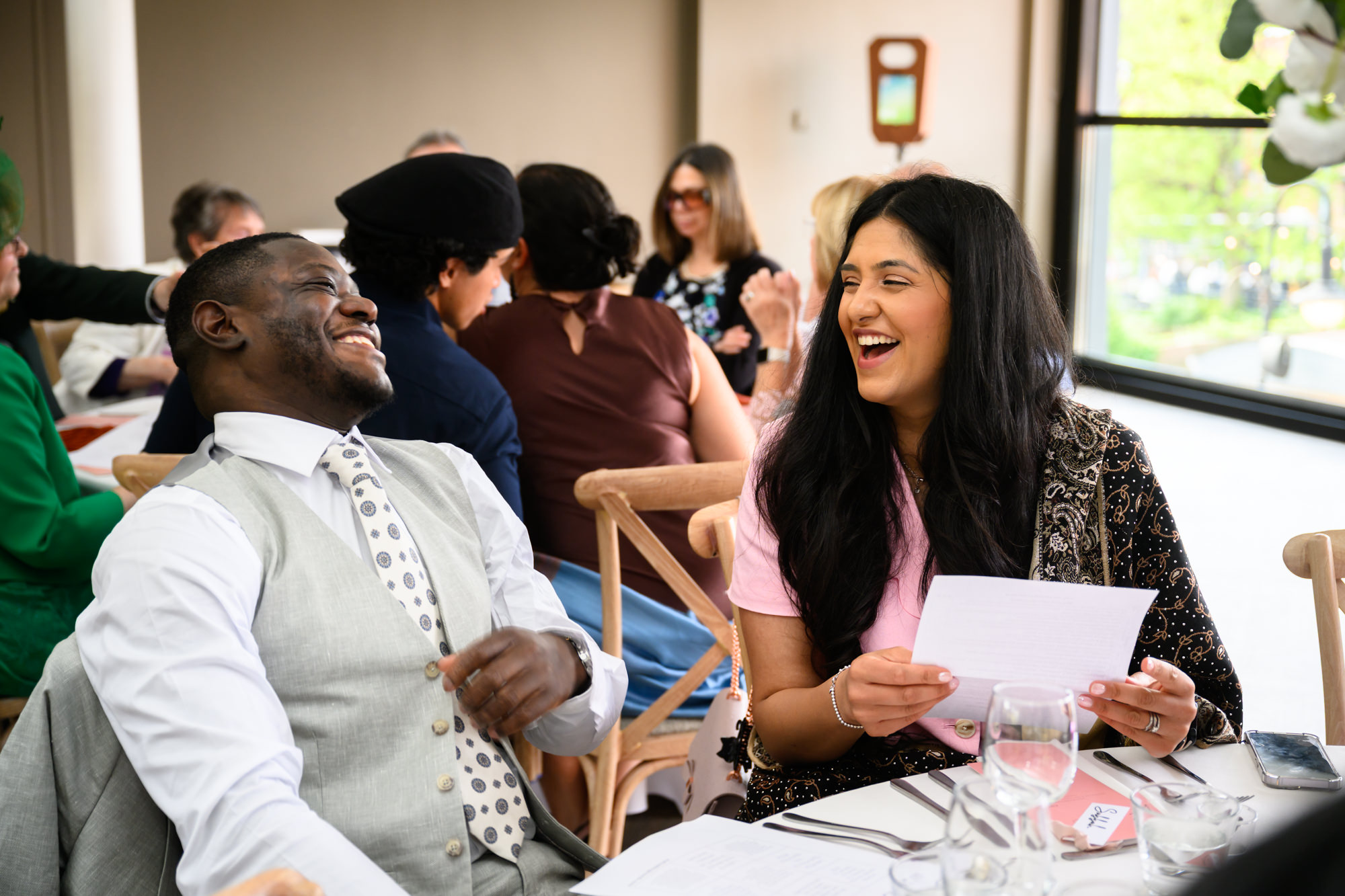 Two wedding guests laughing together at their table during the wedding breakfast in the Merchant Room at The Castlefield Rooms.