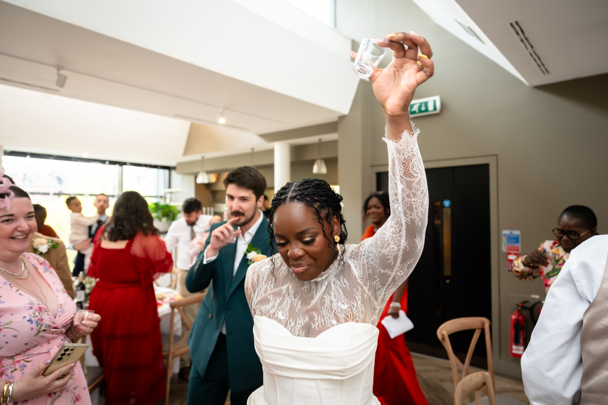 The bride raising a tequila shot glass as she and the groom are announced into the Merchant Room at The Castlefield Rooms for the wedding breakfast.