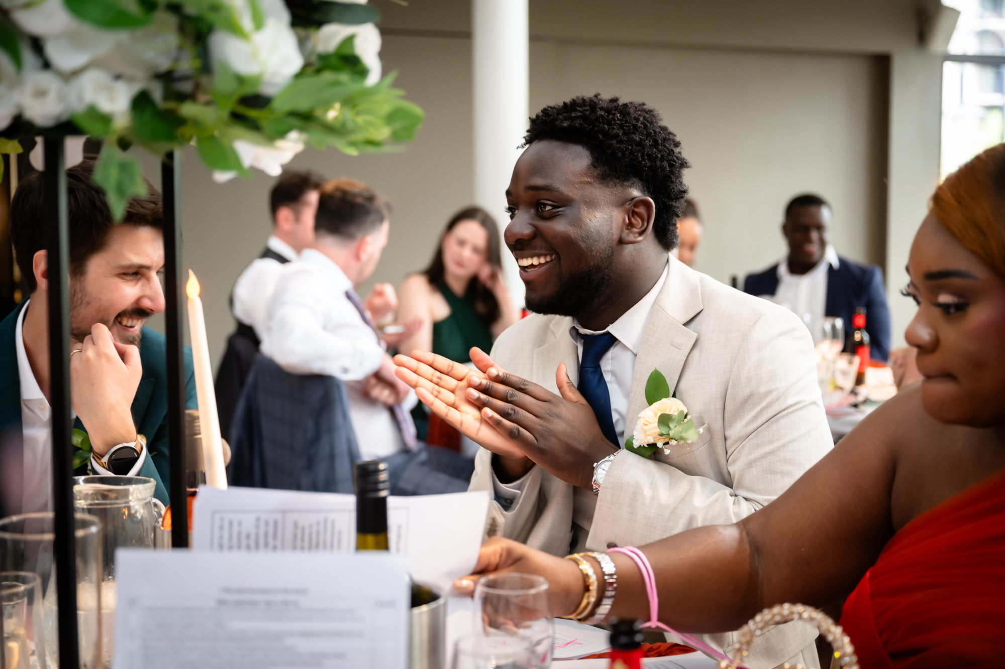 A wedding guest applauding and laughing at his table during the wedding breakfast in the Merchant Room at The Castlefield Rooms.