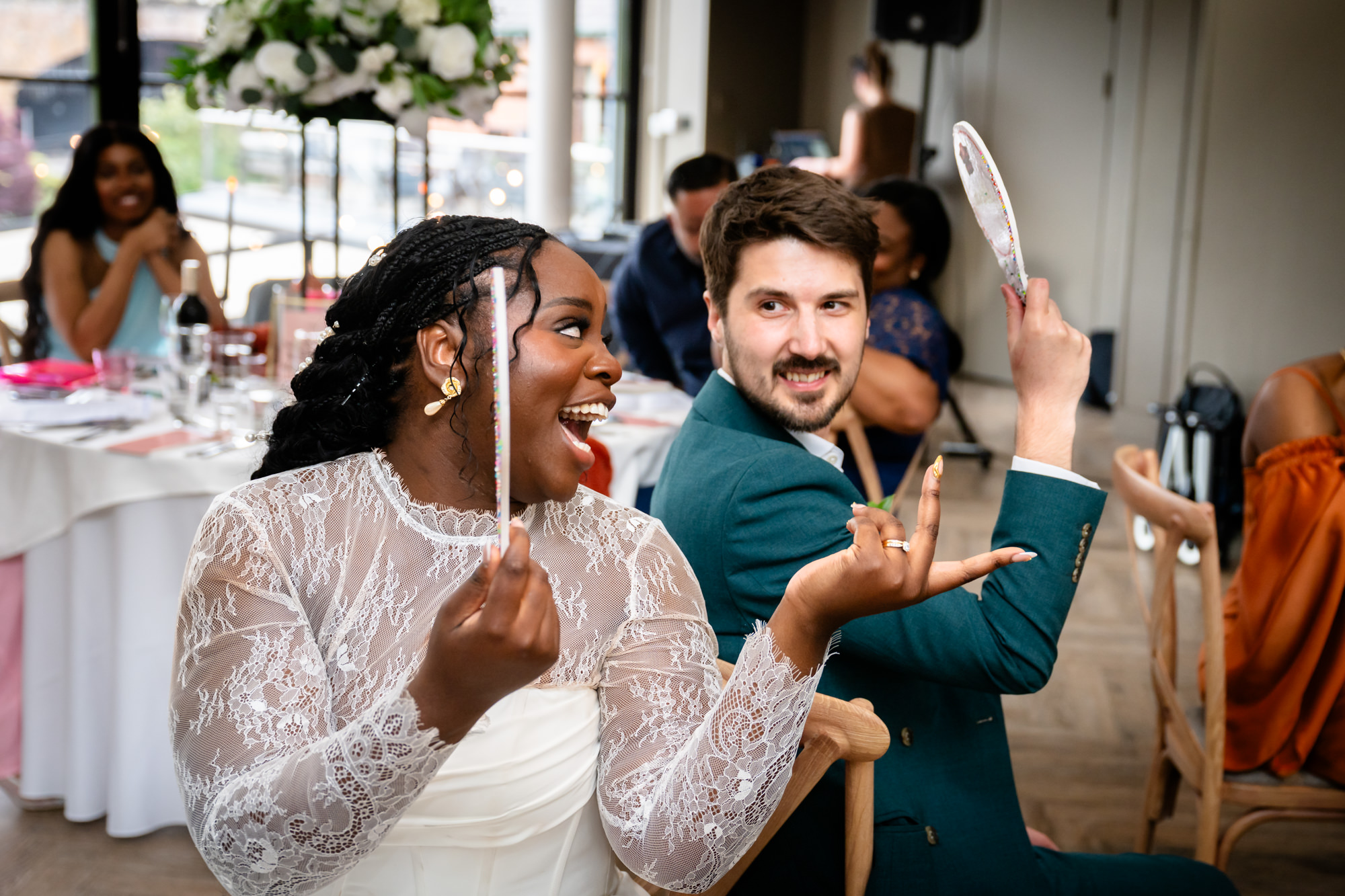 The bride and groom playing Mr and Mrs in the middle of the Merchant Room at The Castlefield Rooms, both holding up their answer paddles during the wedding breakfast.