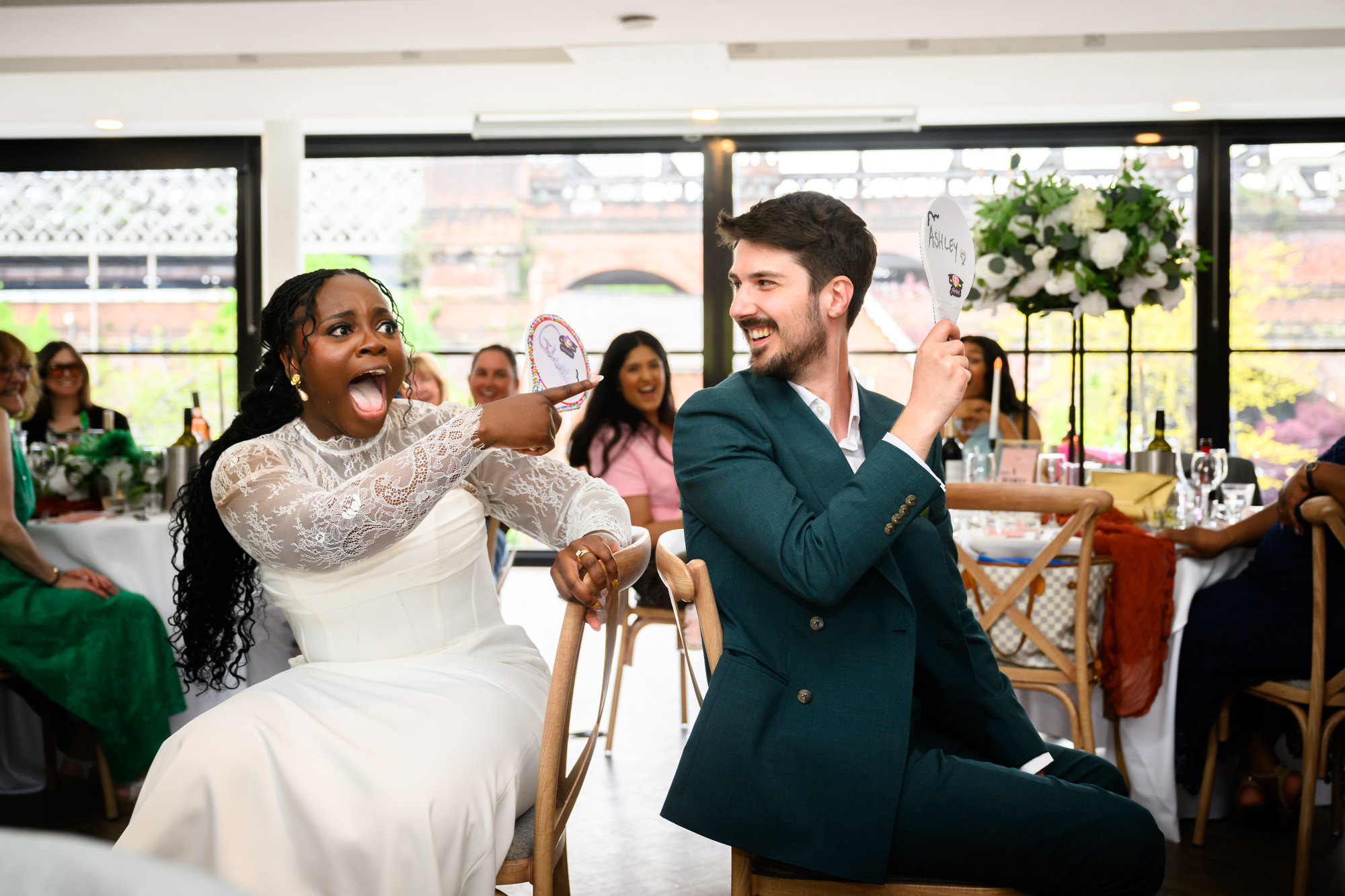 The bride and groom playing Mr and Mrs in the middle of the Merchant Room at The Castlefield Rooms, the bride pointing at the groom's answer in surprise.
