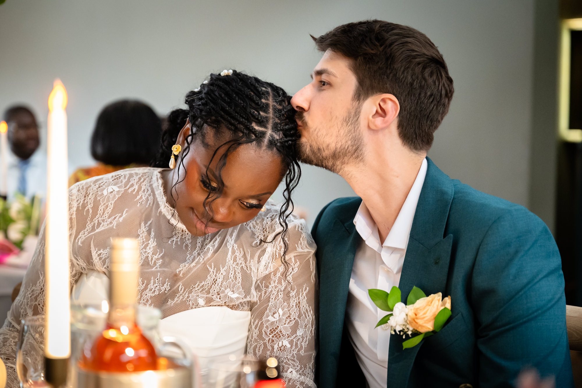 The groom kissing the bride on the head at the top table during the wedding breakfast in the Merchant Room at The Castlefield Rooms.