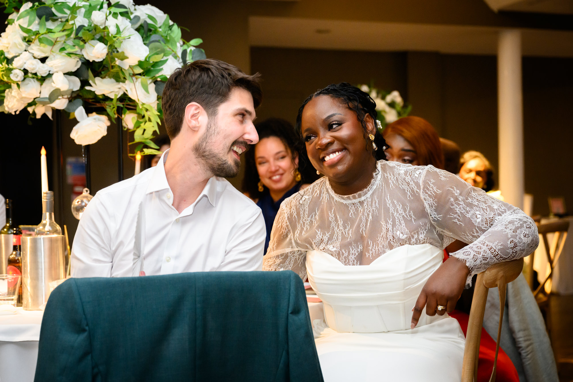 The bride and groom laughing together at the top table during the wedding breakfast in the Merchant Room at The Castlefield Rooms.