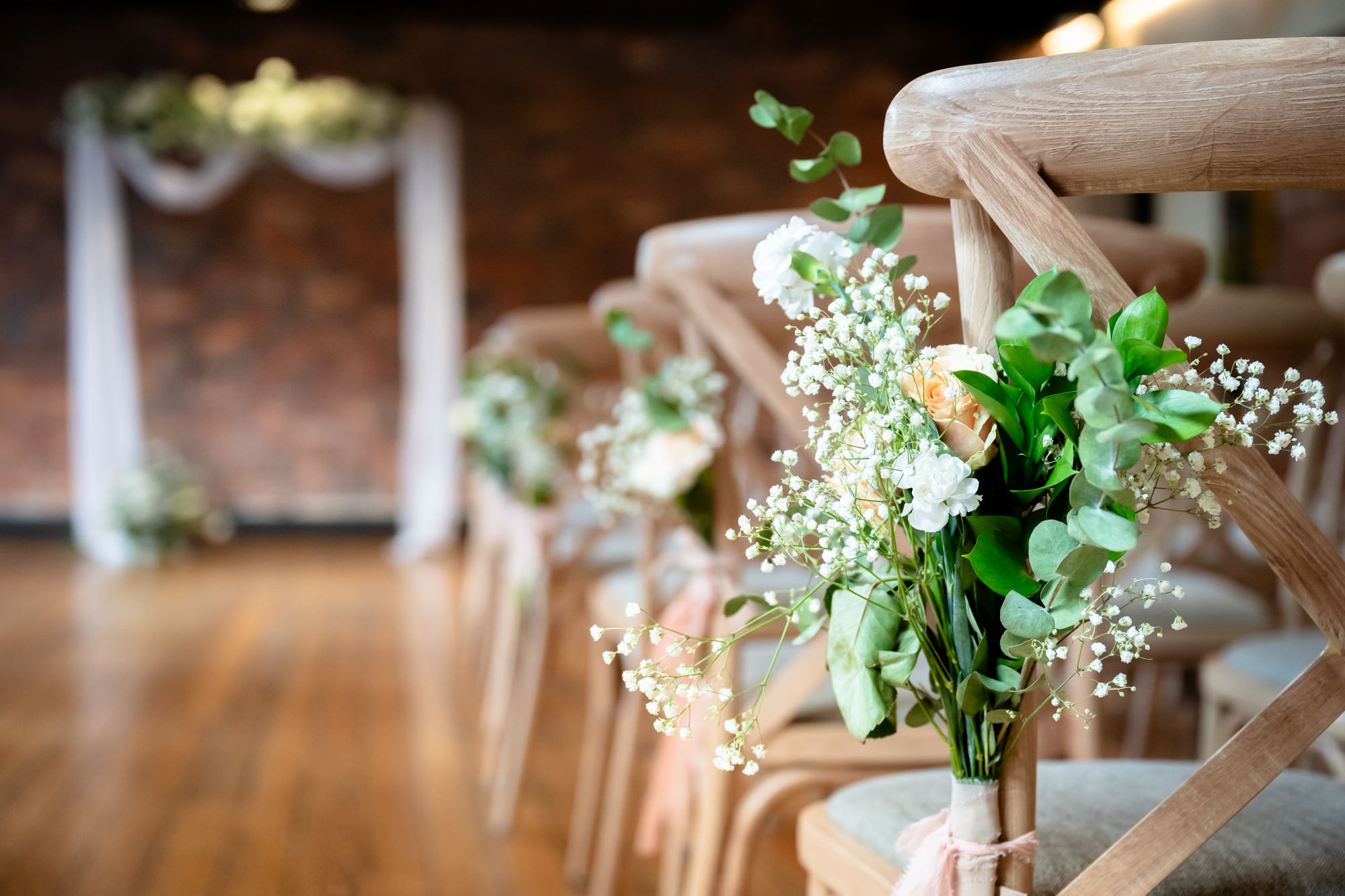 Close-up of a floral chair decoration with peach roses, gypsophila and eucalyptus tied to an aisle chair in the Brindley Room at The Castlefield Rooms.