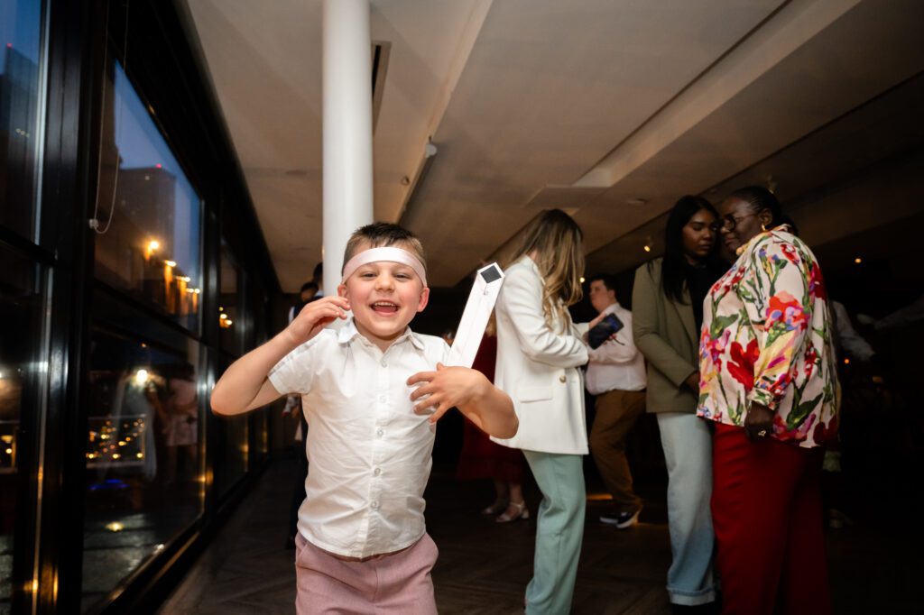 A young wedding guest dancing on the dance floor at The Castlefield Rooms during the evening reception, with a tie wrapped around his head.