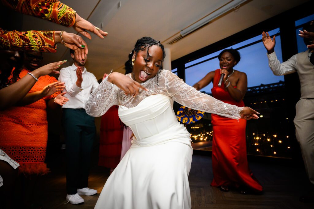 The bride dancing energetically on the dance floor during the evening reception at The Castlefield Rooms, surrounded by guests and a bridesmaid singing into a microphone.