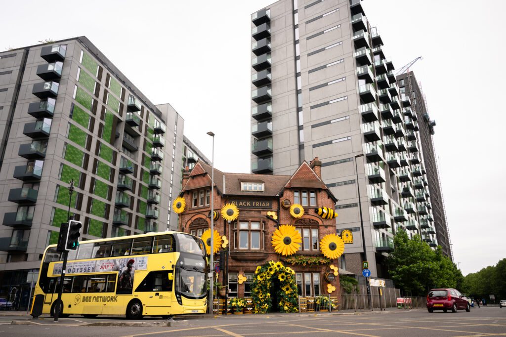 Black Friar pub in Salford decorated with giant sunflower sculptures on the outside, with a yellow bus passing by