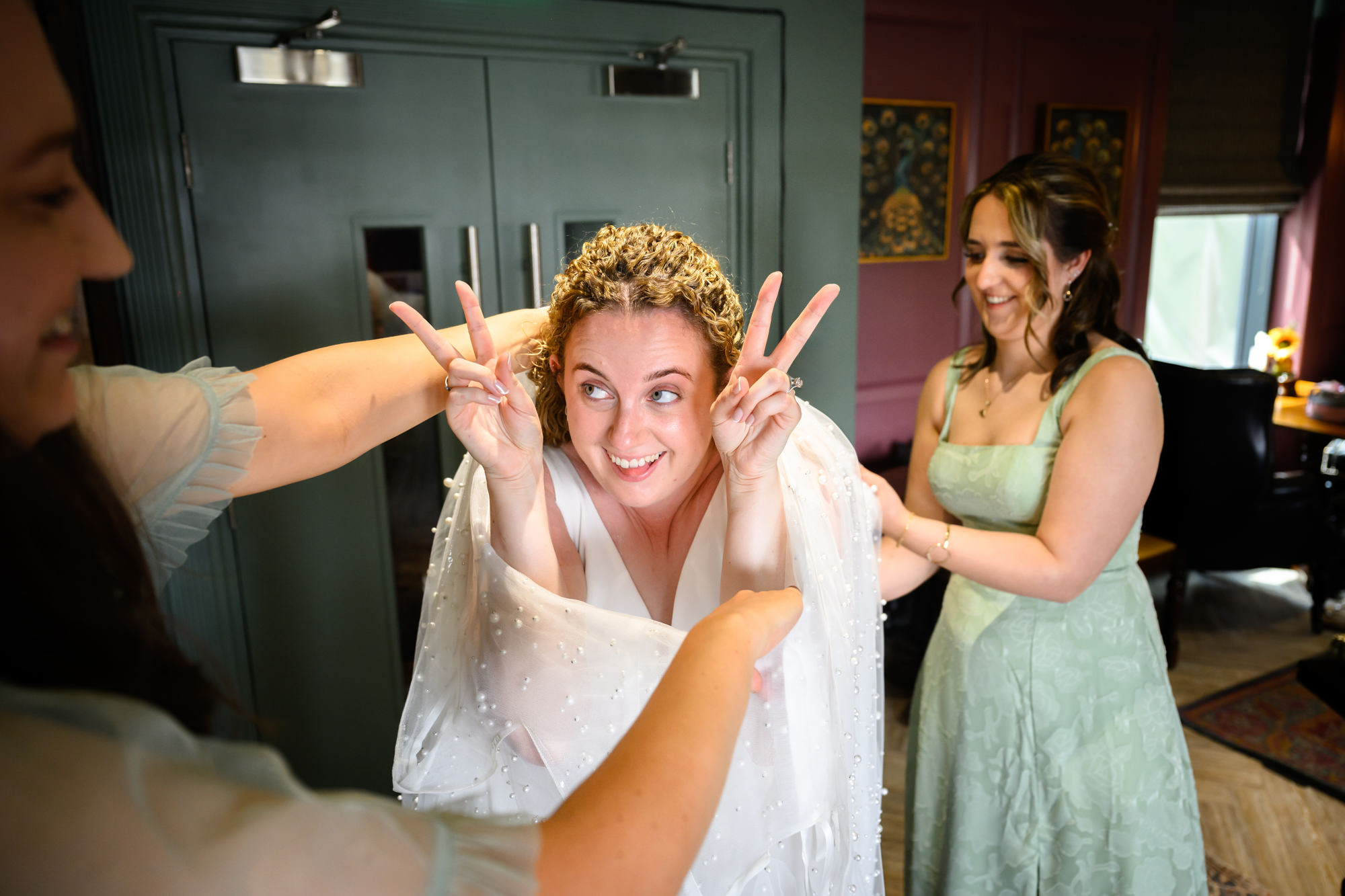 Bride making a peace sign while bridesmaids help adjust her dress