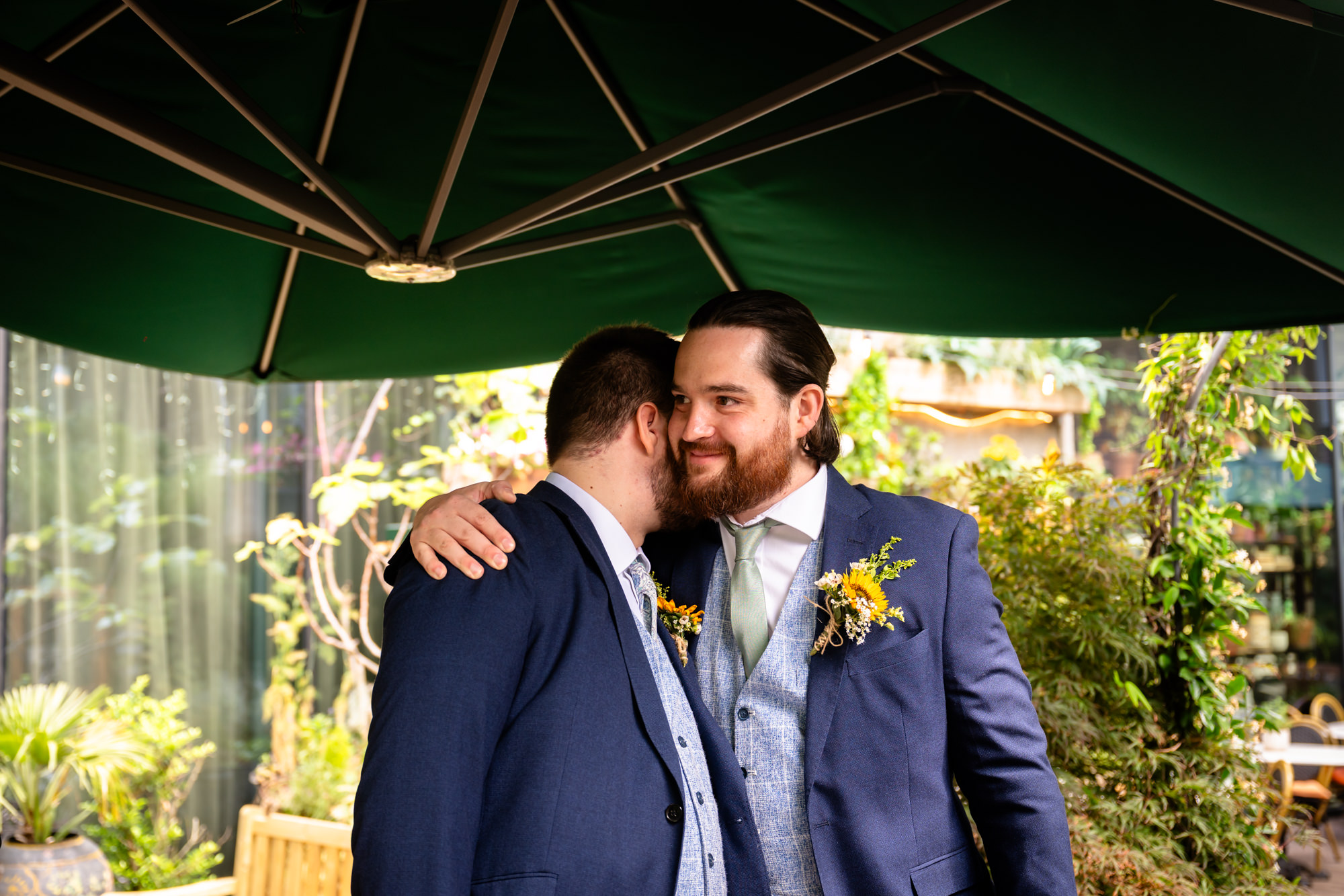 Groom and his best man hugging under a green parasol before the ceremony