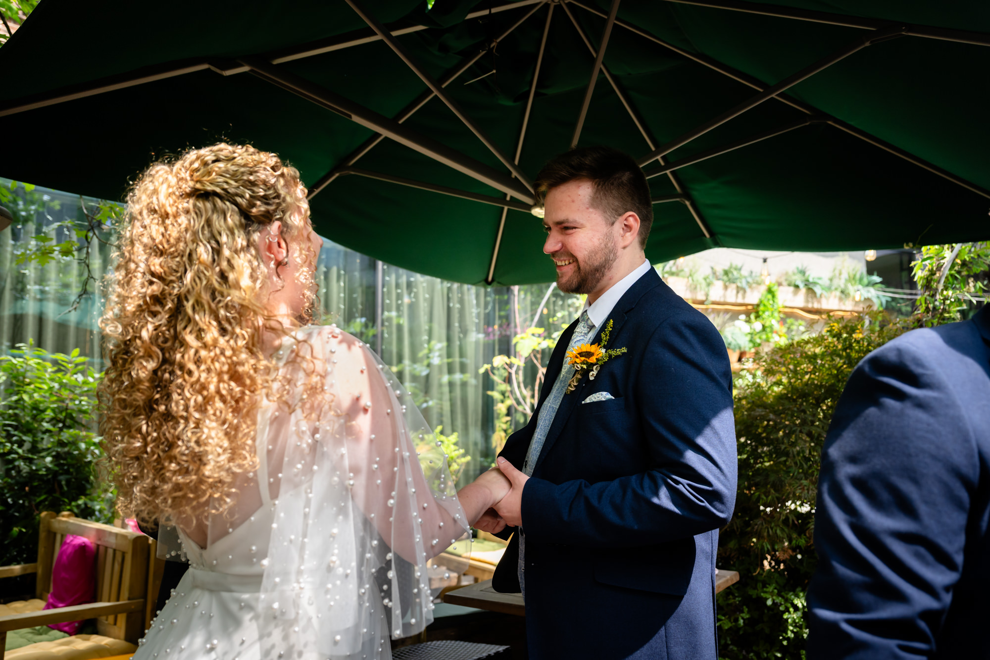 Bride and groom holding hands and smiling under a parasol during the ceremony