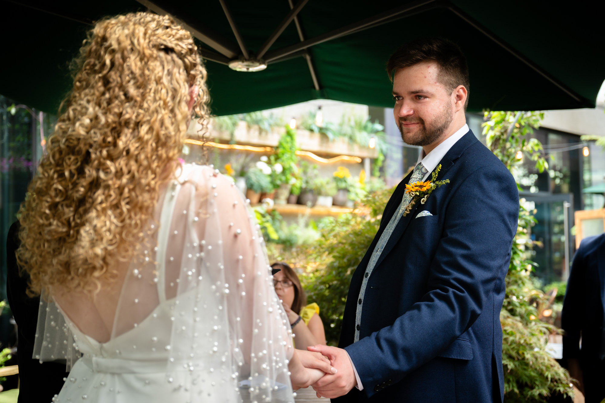 Bride and groom holding hands during the vows, the back of the bride's dress visible